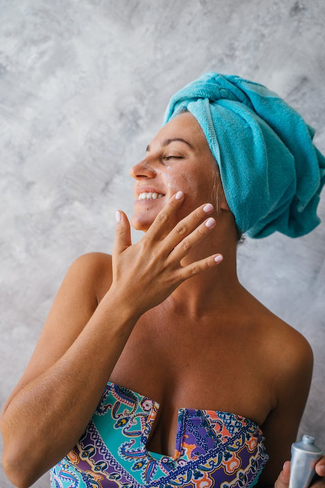 A Woman with A Towel Wrapped Around Her Head Is Applying Lotion to Her Face — Rejuved in Bateau Bay, NSW