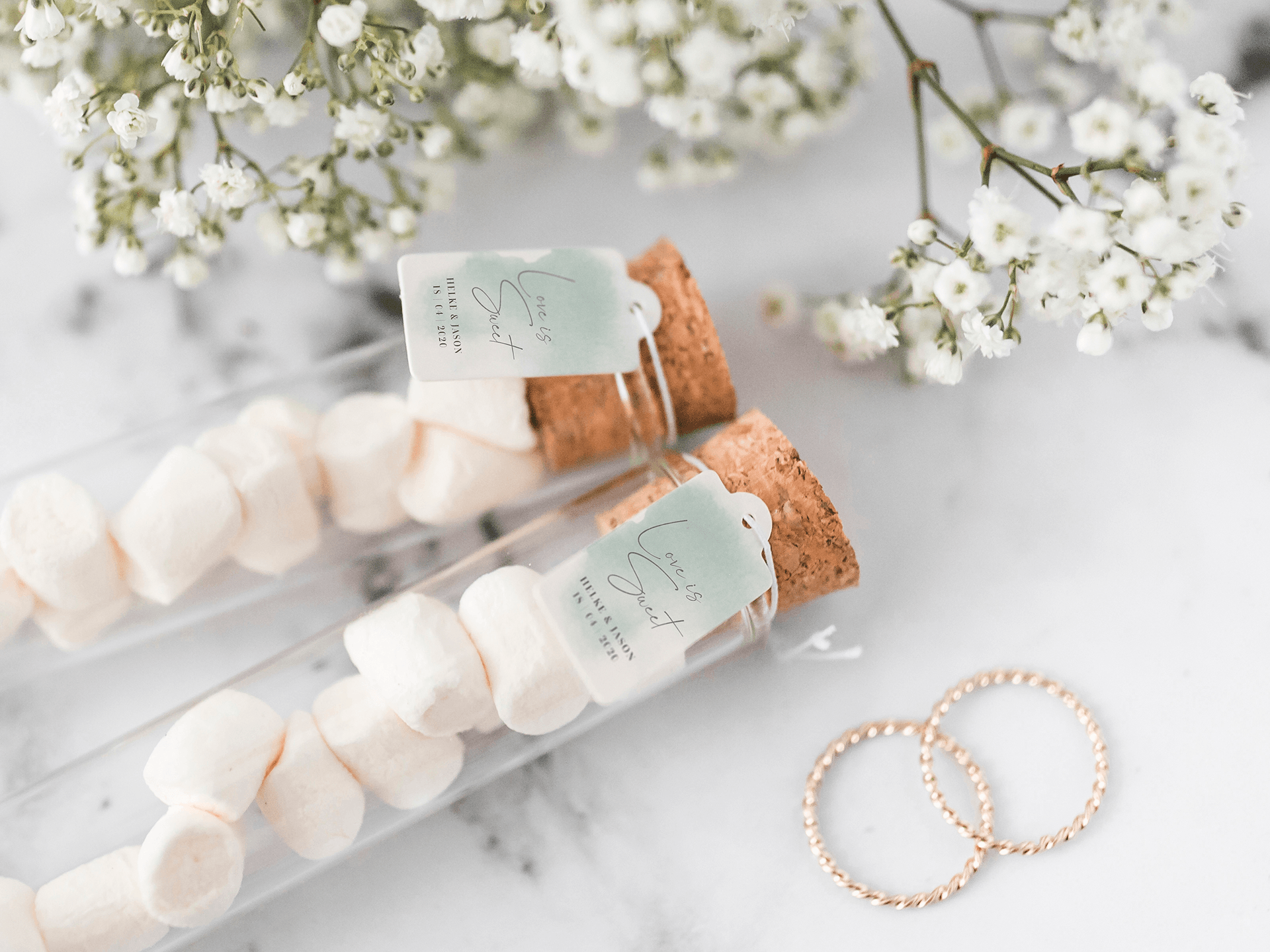 Gastgeschenk Hochzeit Gastgeschenk Hochzeit, 2 Reagenzgläser mit Süßigkeiten gefüllt und mit Schildchen dekoriert, daneben Schleierkraut und Eheringe