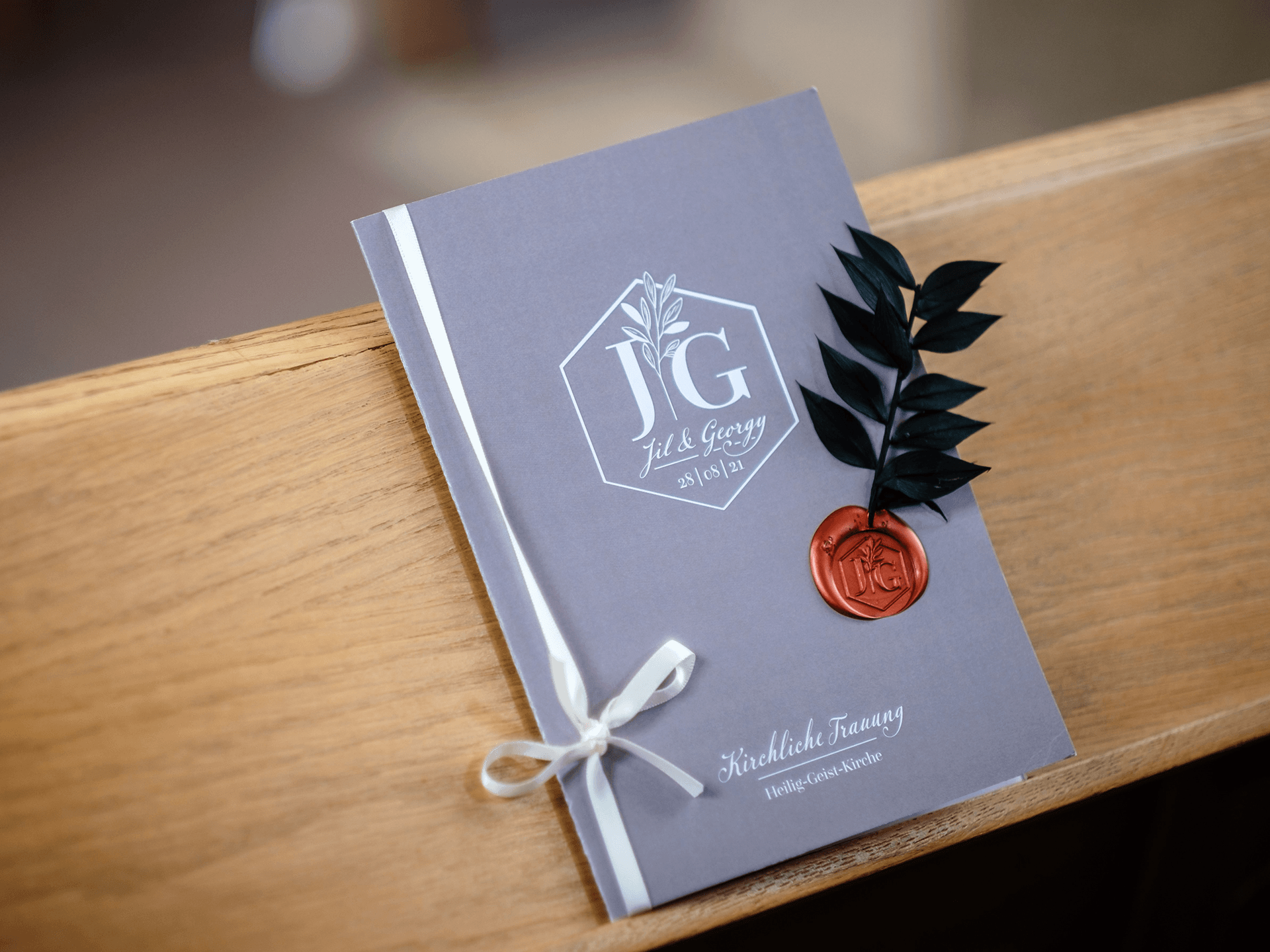 Kirchenheft auf Kirchenbank ausgelegt, taupe mit Hochzeitslogo, Seidenband und personalisiertem Siegel