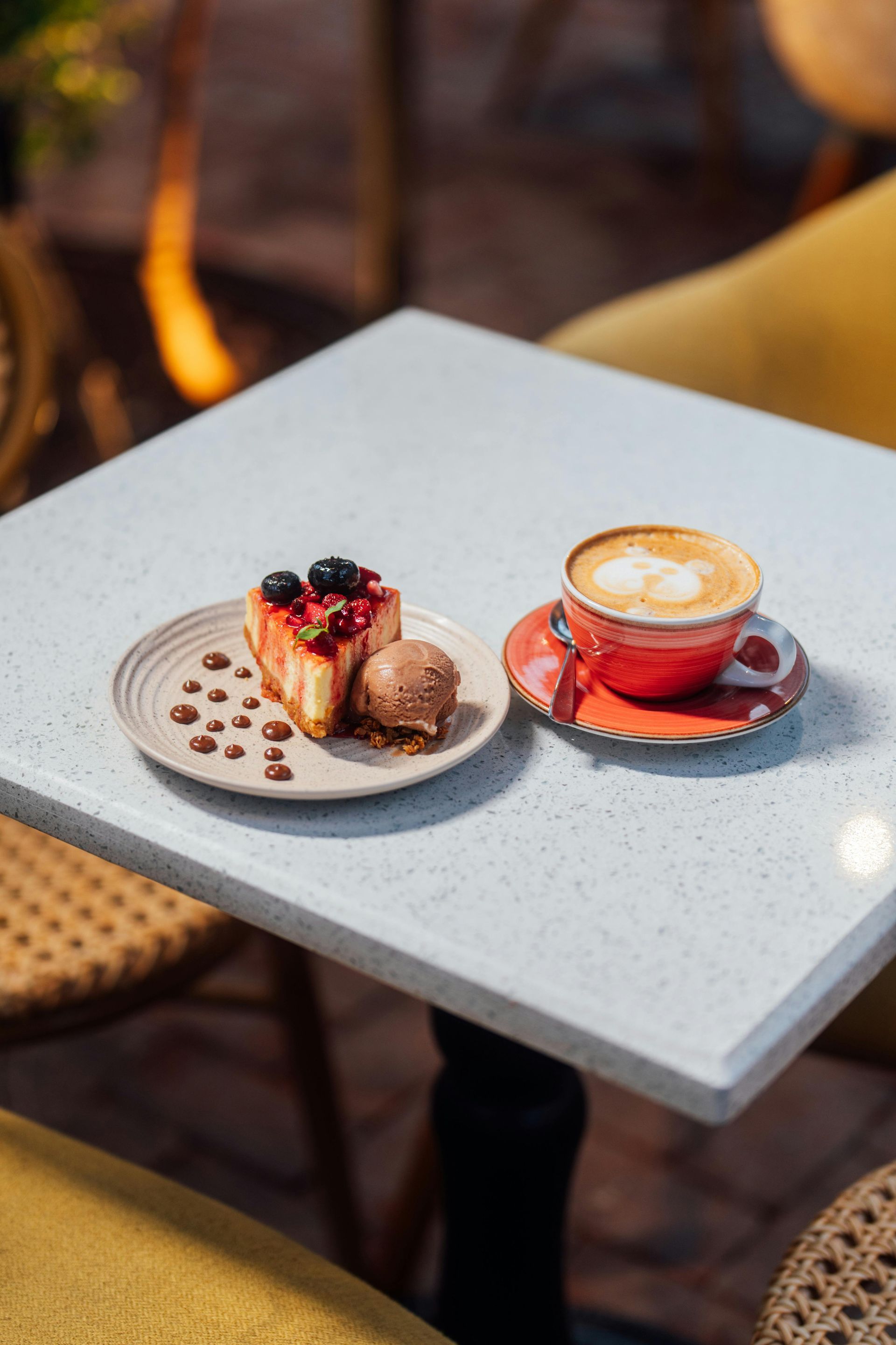 Een plakje taart met bessen en een bolletje ijs op een bordje, naast een kopje koffie op tafel.