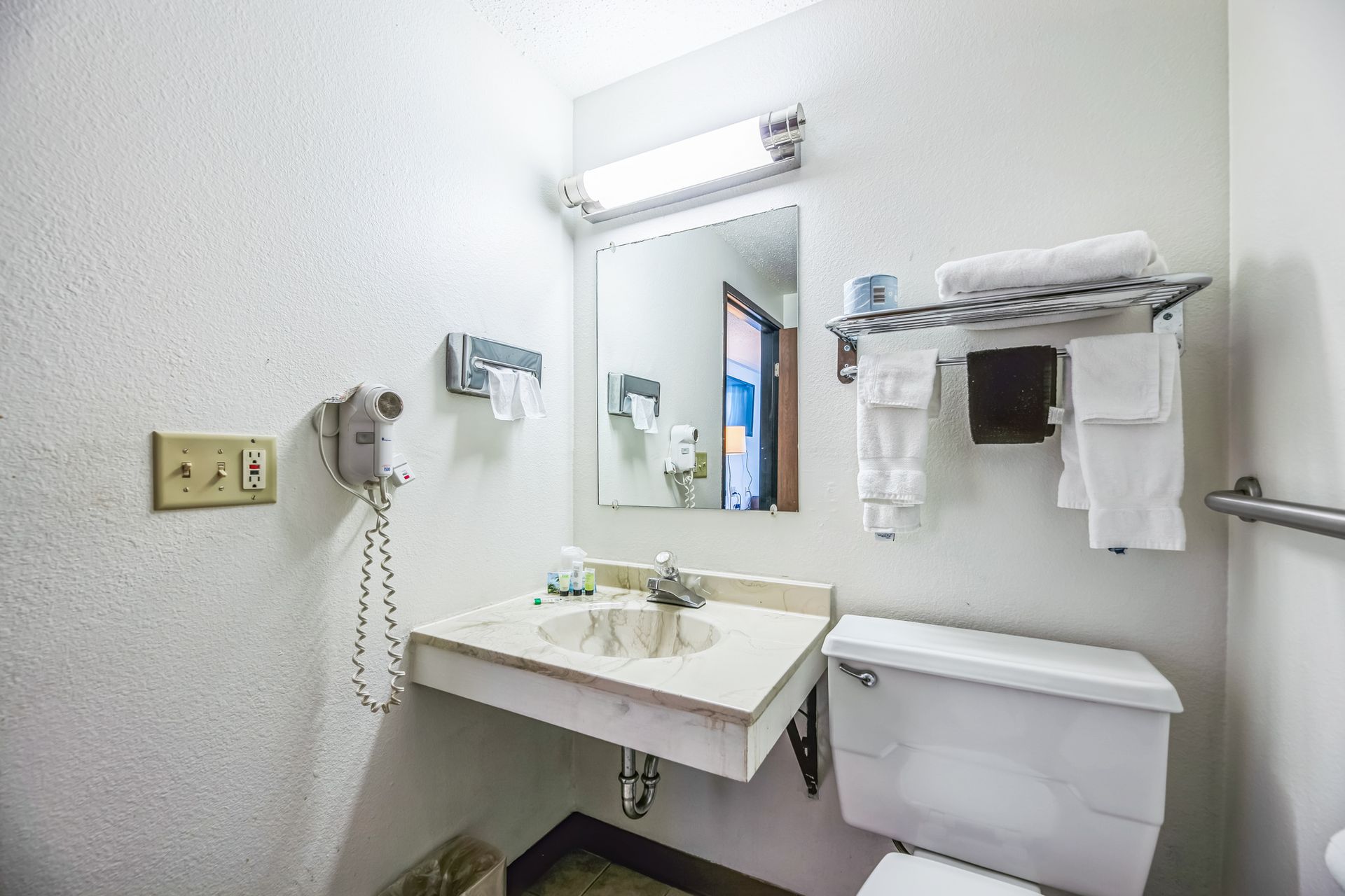 Small bathroom with sink, mirror, toilet, towel rack. Wall-mounted hairdryer on the left.