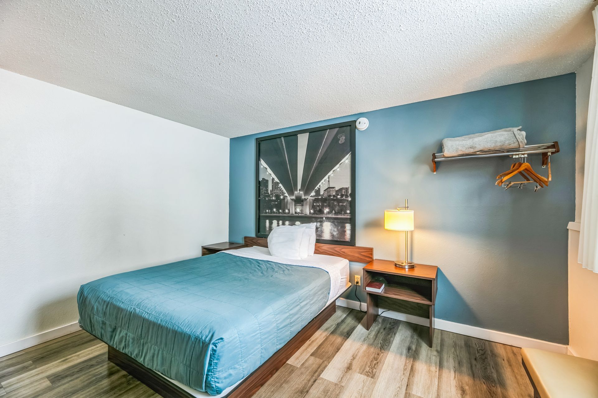 Bedroom with a bed, nightstand, and wall art; blue and white walls; wood-look floor.