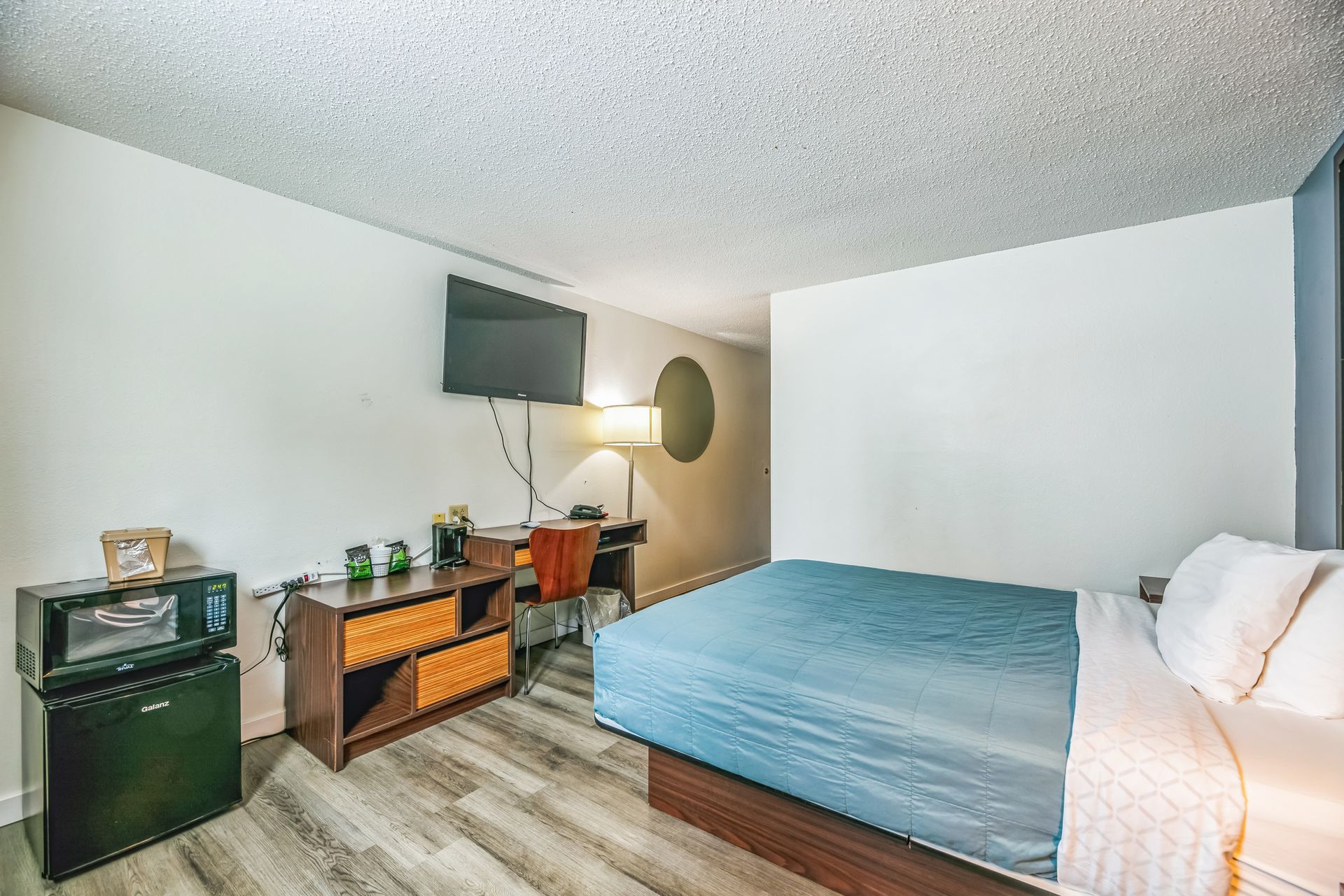Hotel room interior with bed, desk, TV, microwave, and mini-fridge.