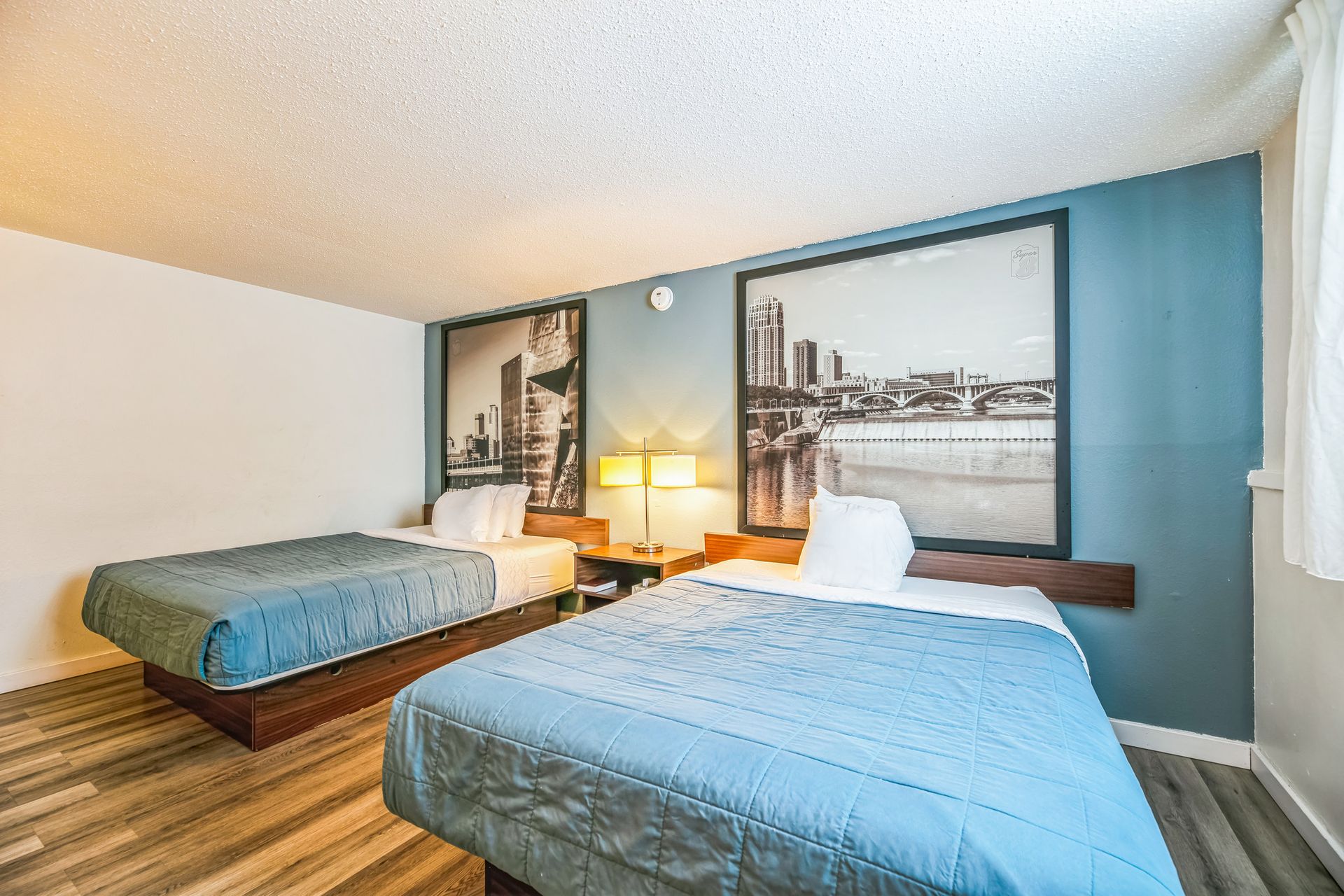 Two twin beds in a room with cityscape art, blue bedspreads, and wooden headboards.