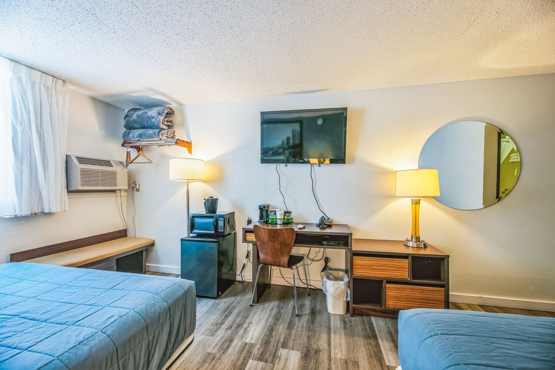Motel room with two beds, desk, TV, microwave, and round mirror.