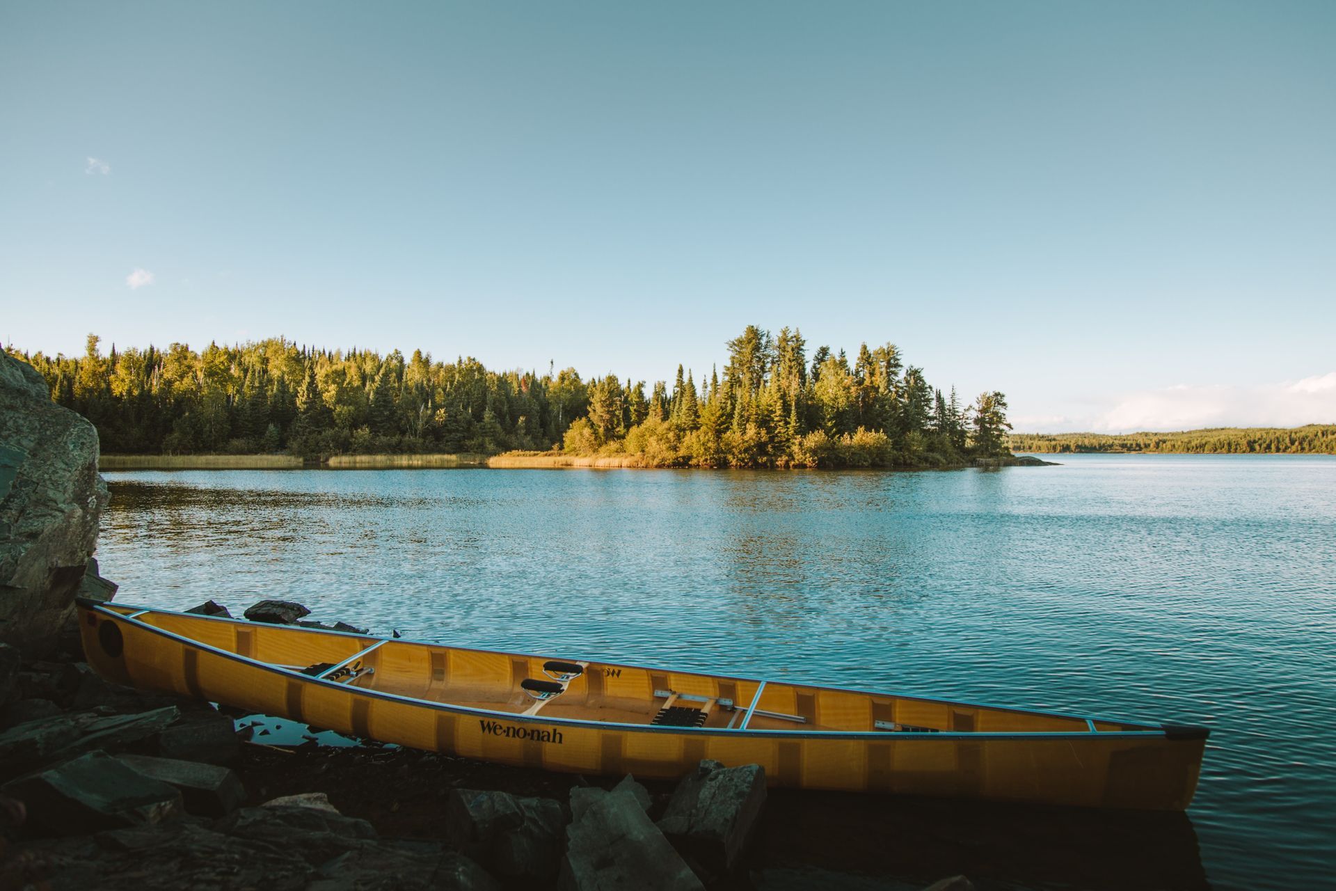 Yellow canoe on shore of calm lake, island with trees in background, sunny day.