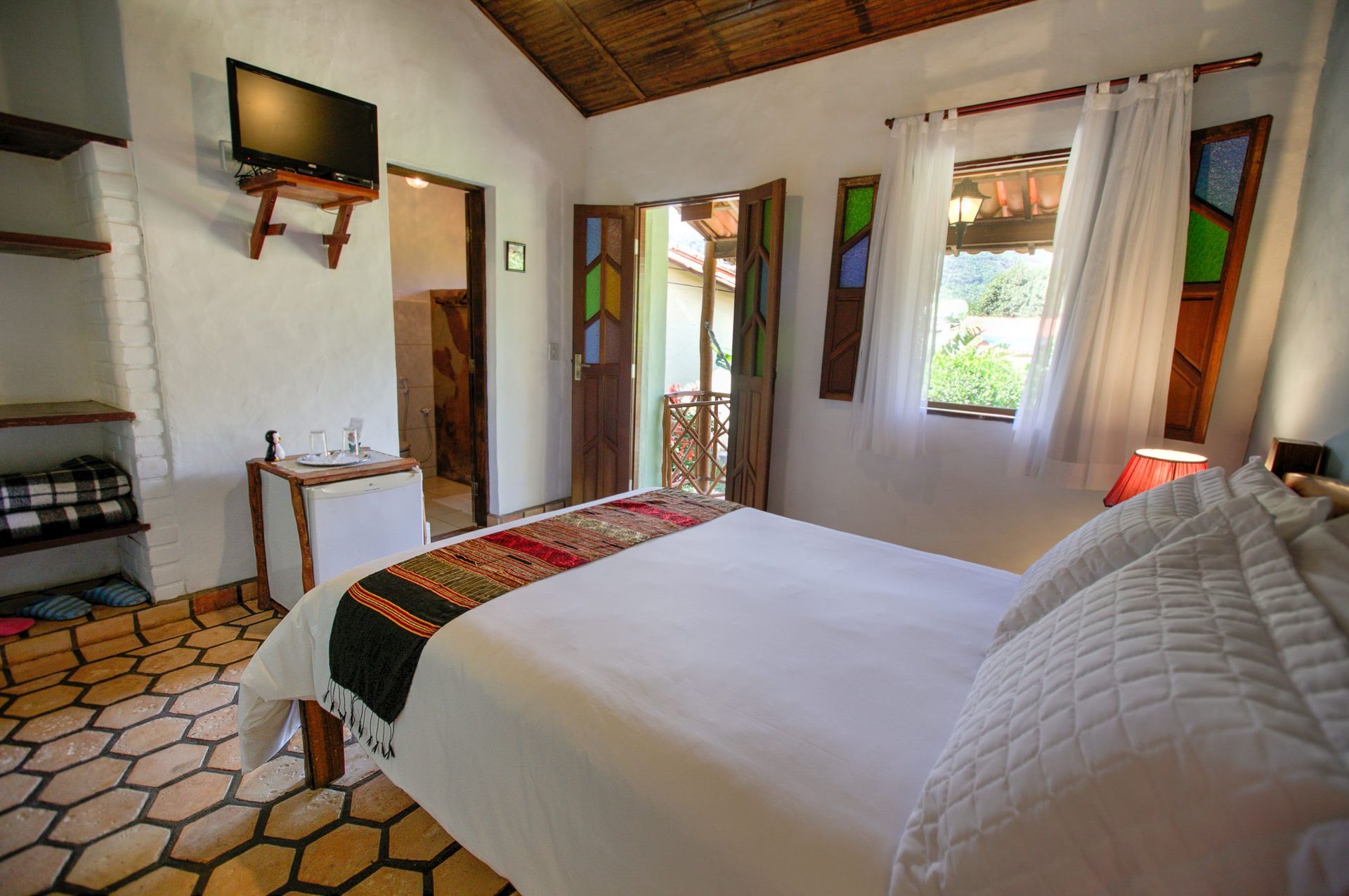 Um quarto com uma cama, televisão e vitrais.