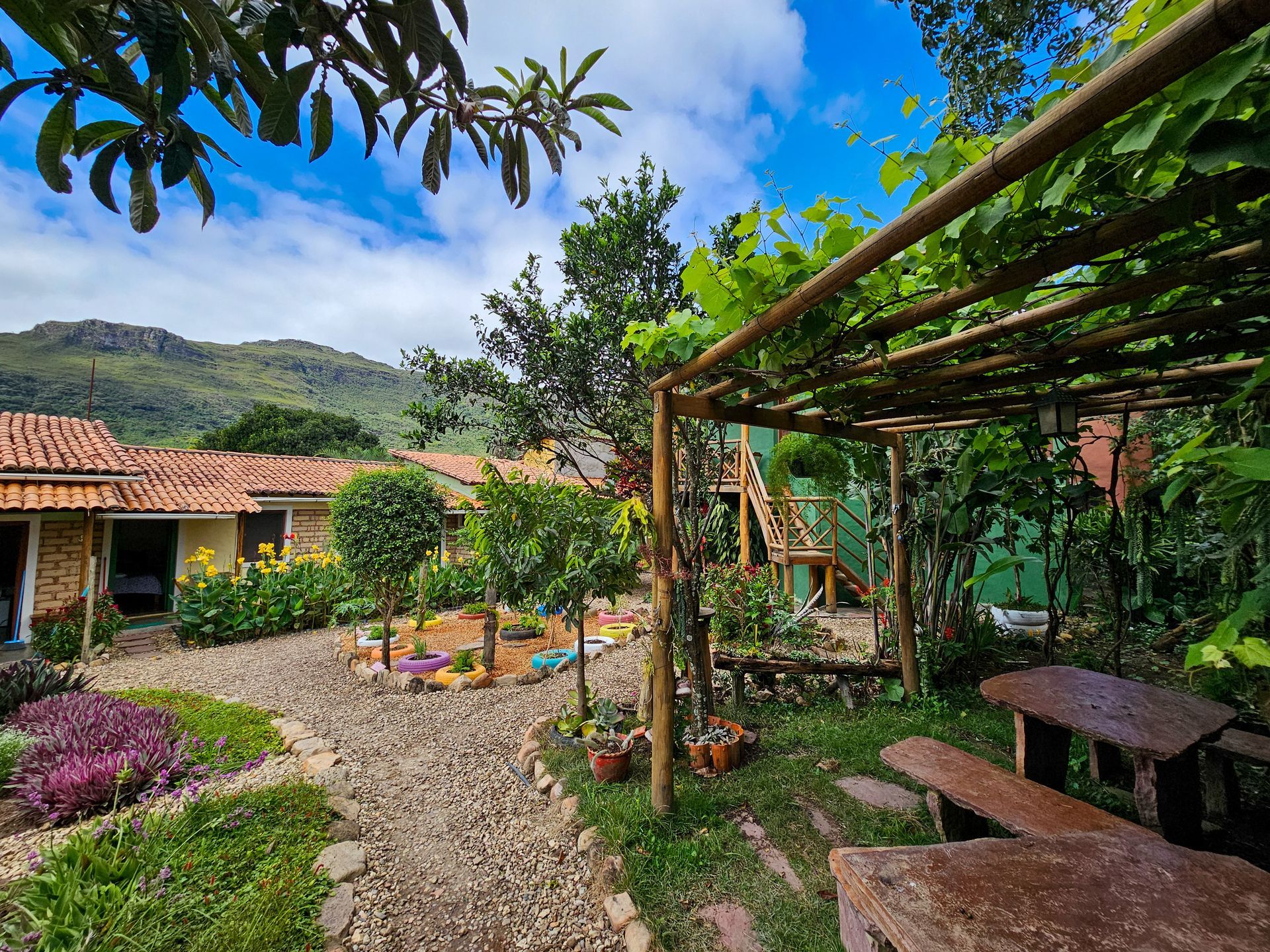 Um jardim com flores e pedras em frente a uma casa com montanhas ao fundo.