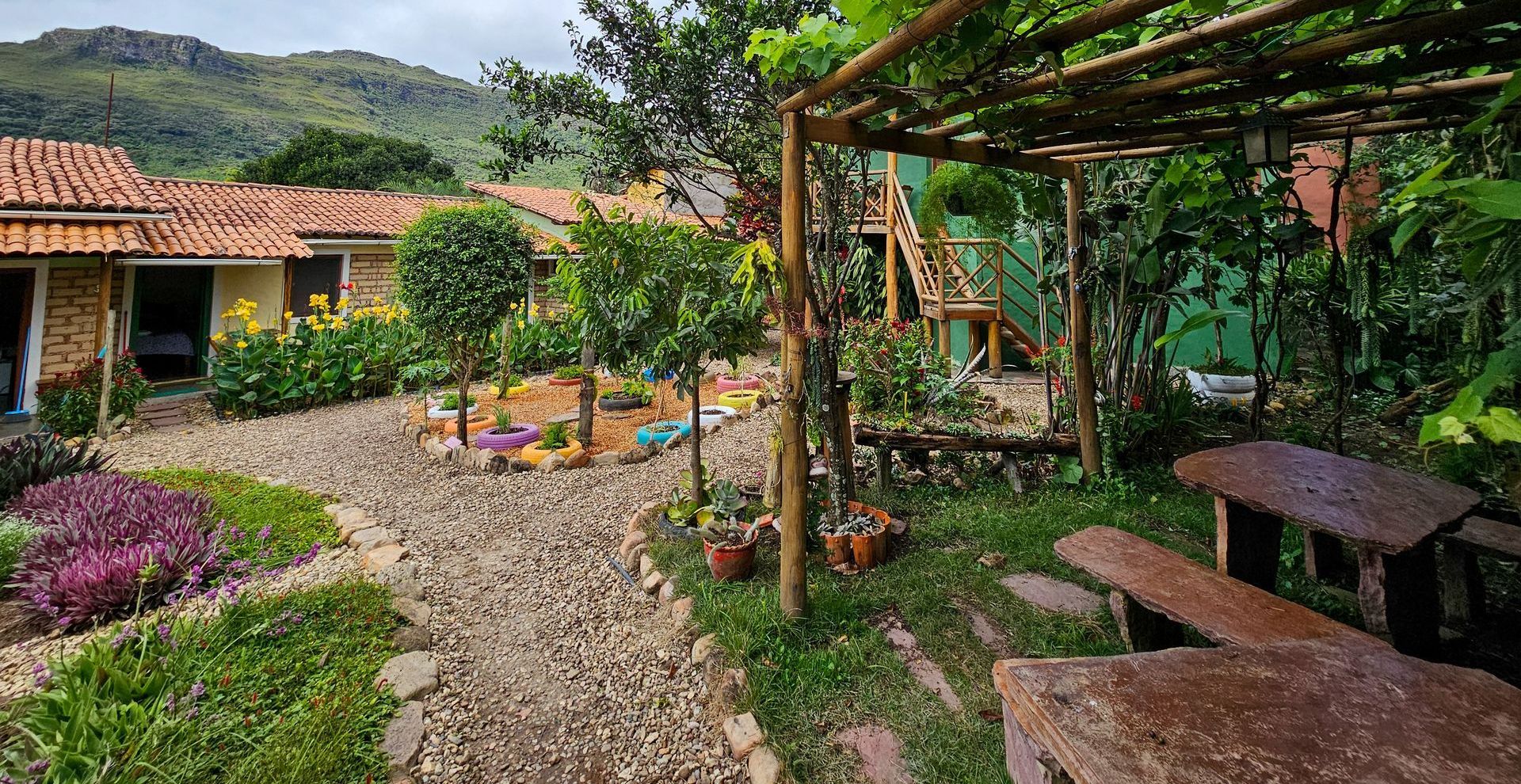 Um jardim com flores e pedras em frente a uma casa com montanhas ao fundo.