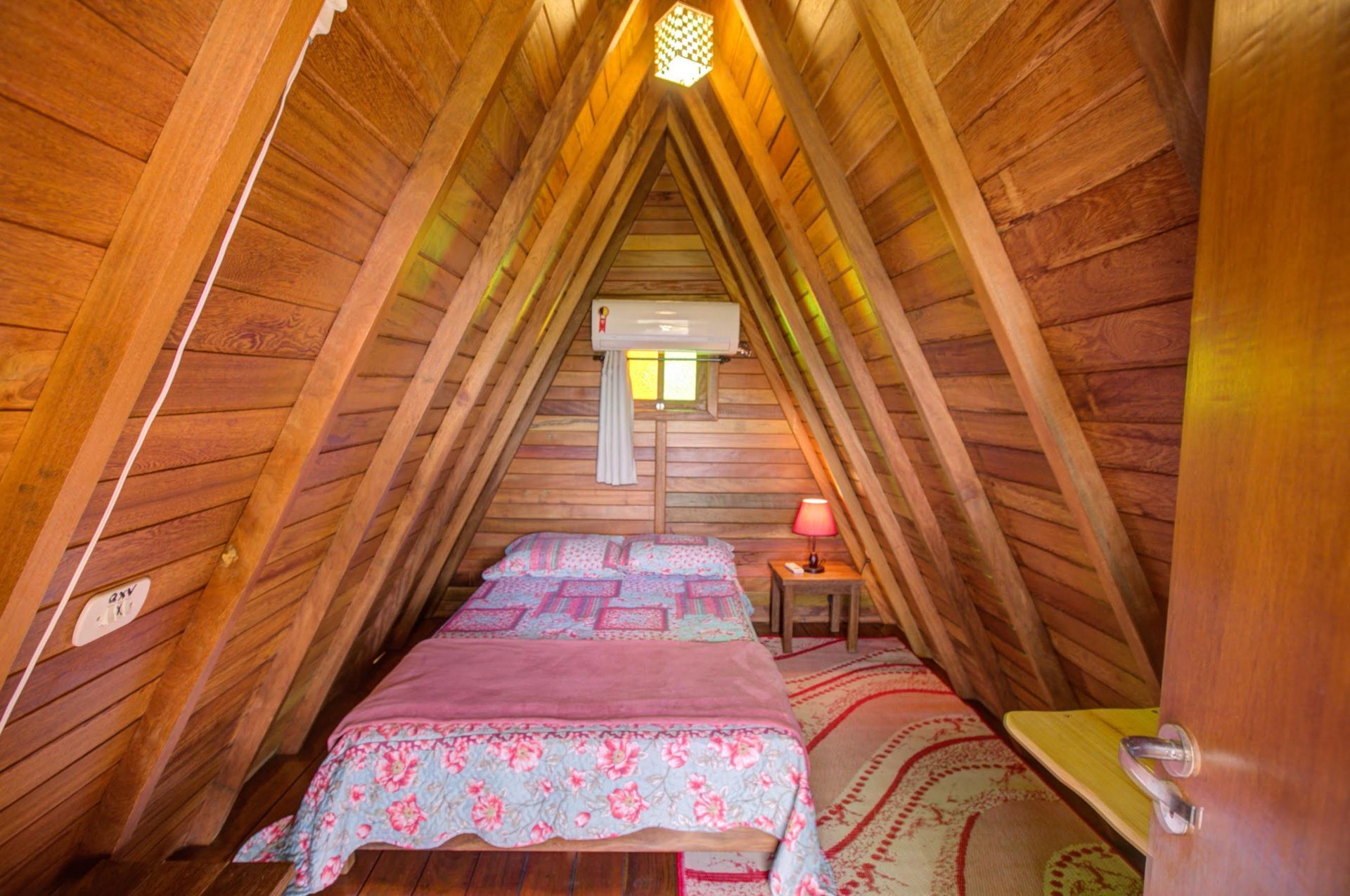 Há uma cama no sótão de uma cabana de madeira.