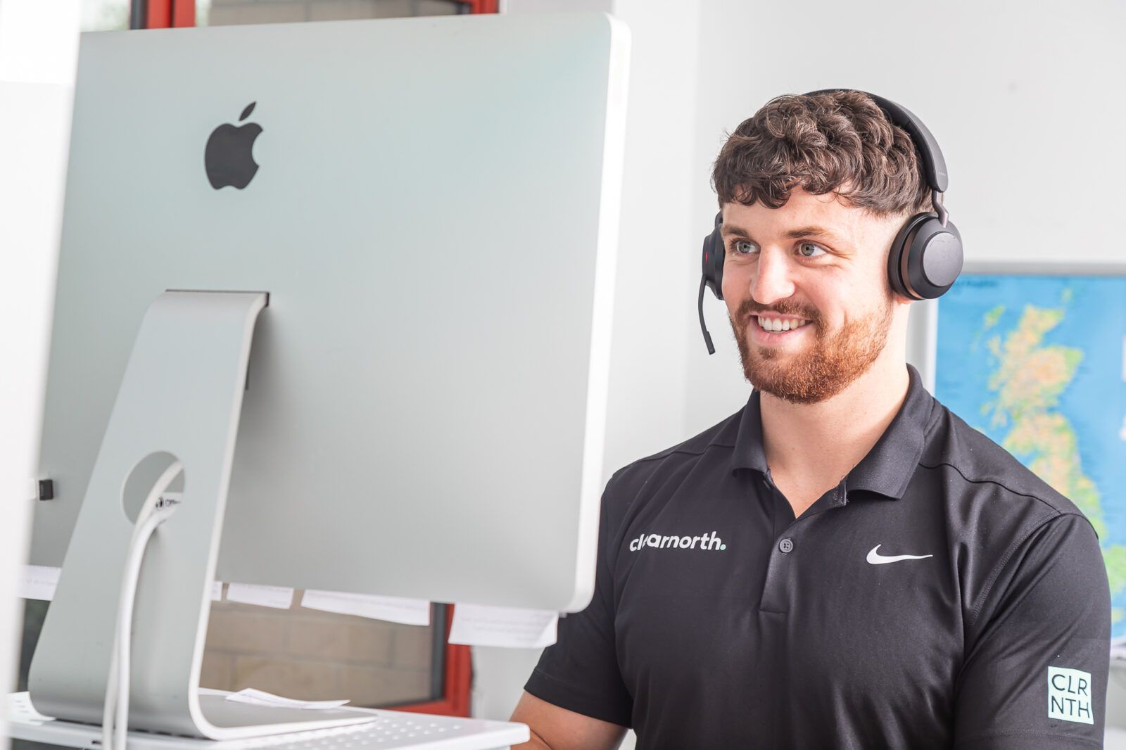 A woman wearing glasses and a green polka dot shirt is holding her finger to her lips.