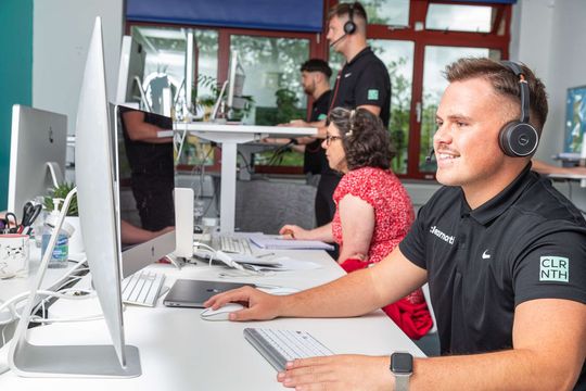 A man wearing headphones is sitting at a desk in front of a computer.
