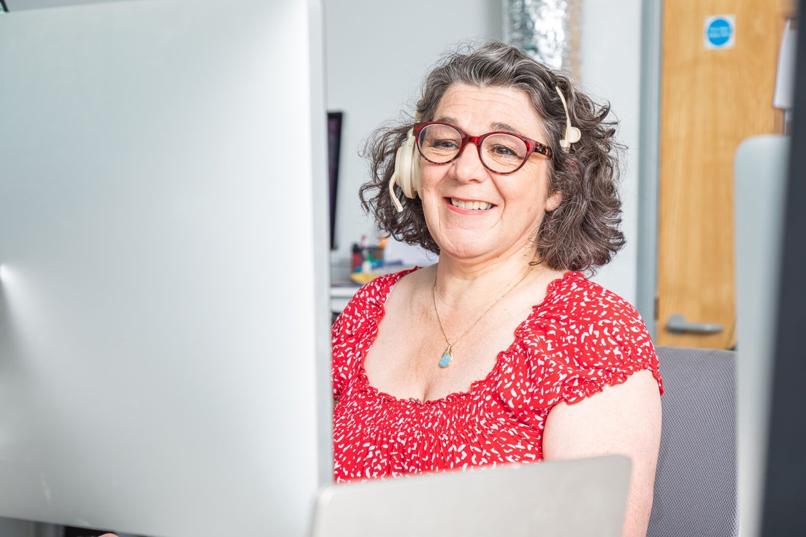 A woman is smiling while sitting in front of a computer monitor.