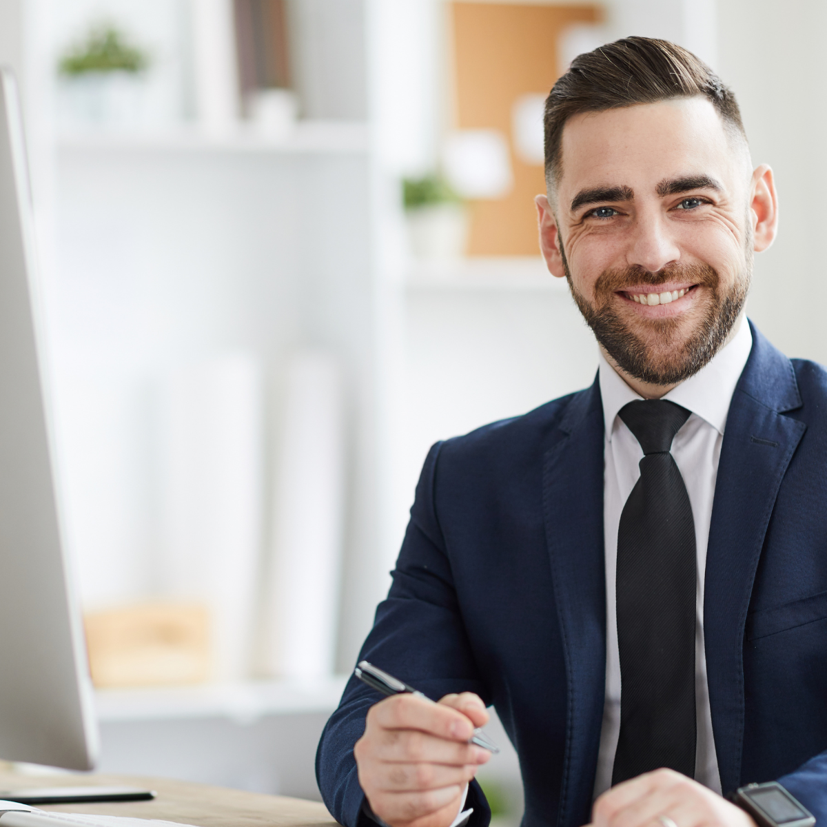 A man in a suit and tie is sitting at a desk with a pen in his hand.
