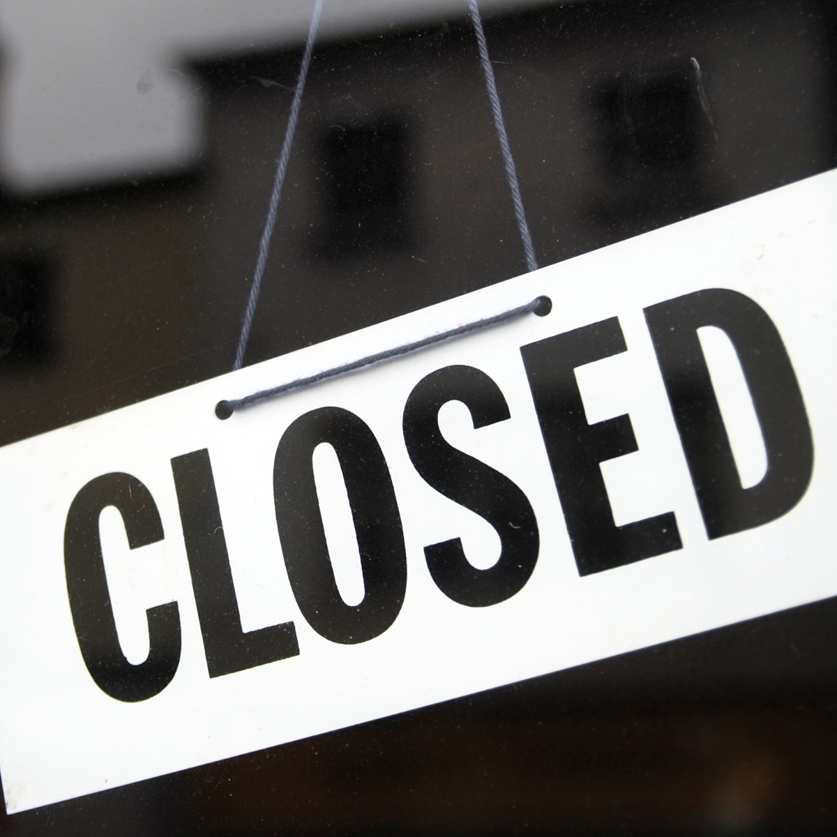 A closed sign hangs from a string in front of a building