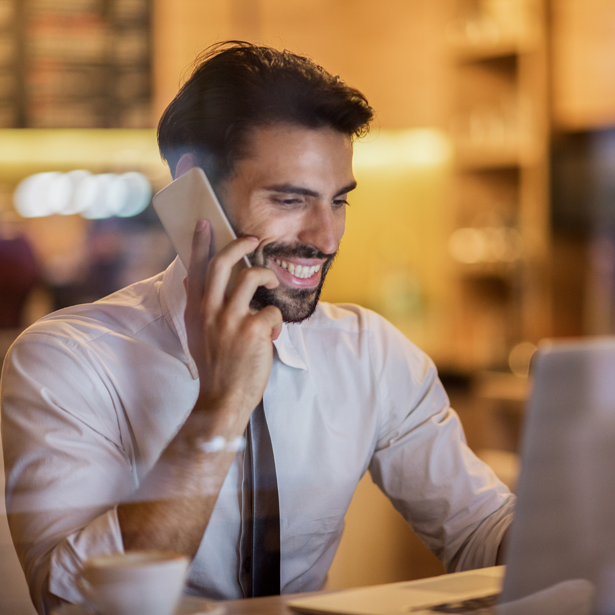 A man is talking on a cell phone while using a laptop