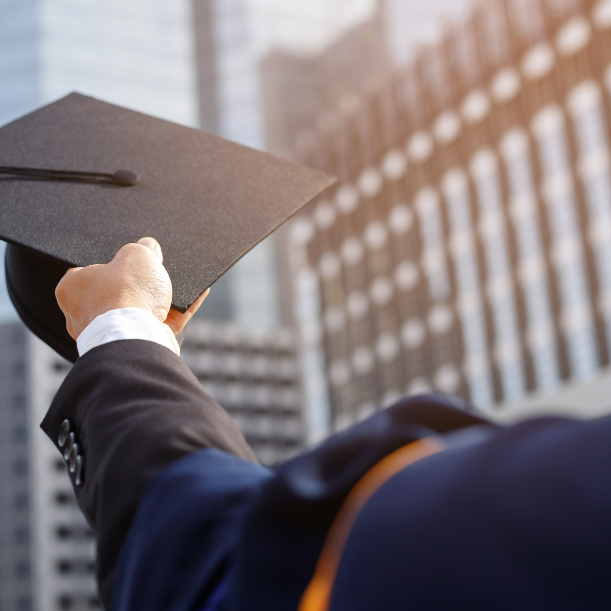 A man in a suit is holding a graduation cap in his hand
