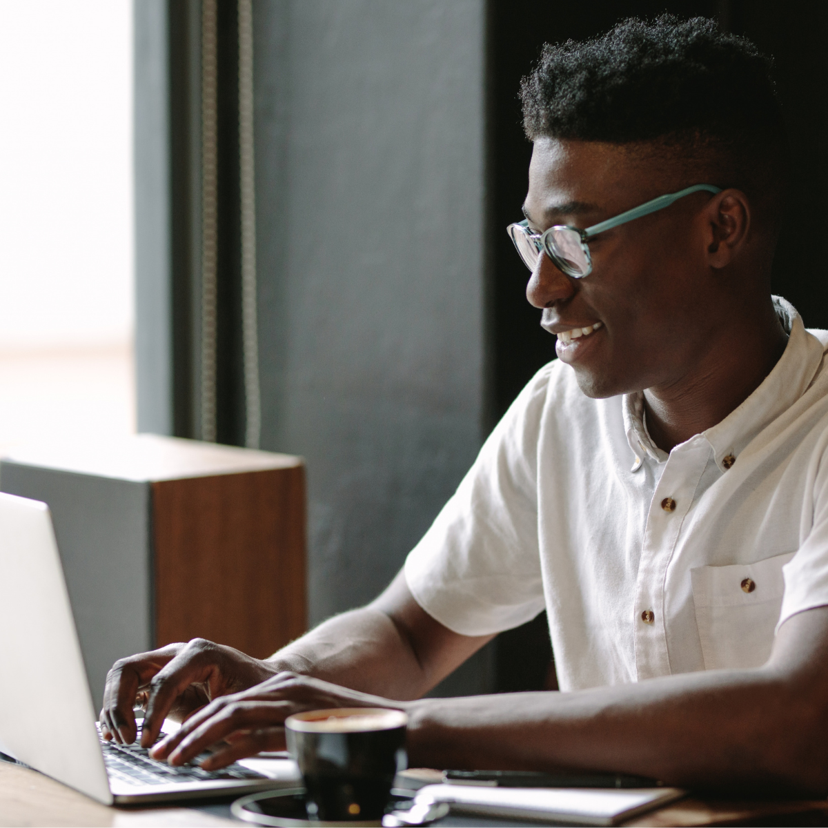 A man wearing glasses is typing on a laptop computer