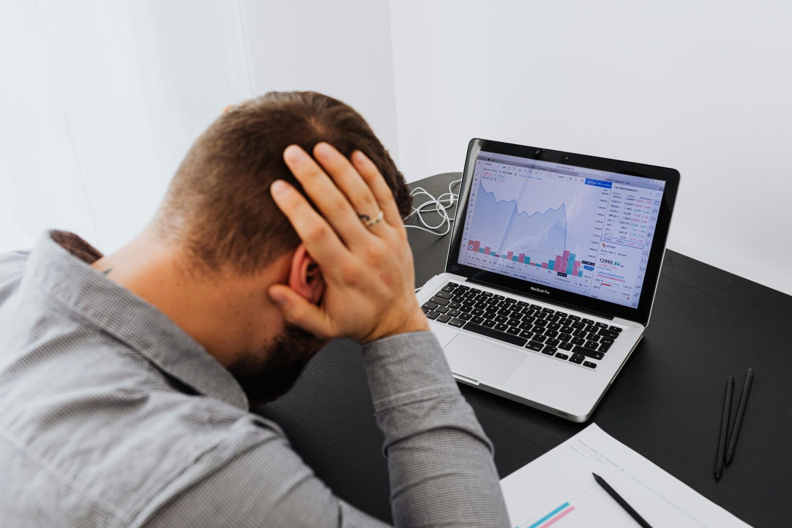 A man is sitting at a desk with his head in his hands in front of a laptop computer.
