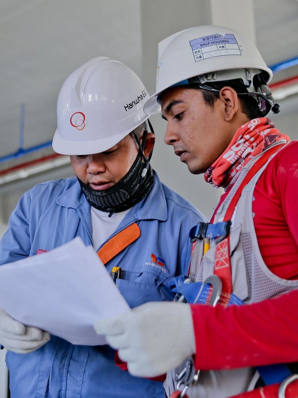 Two men wearing hard hats are looking at a piece of paper