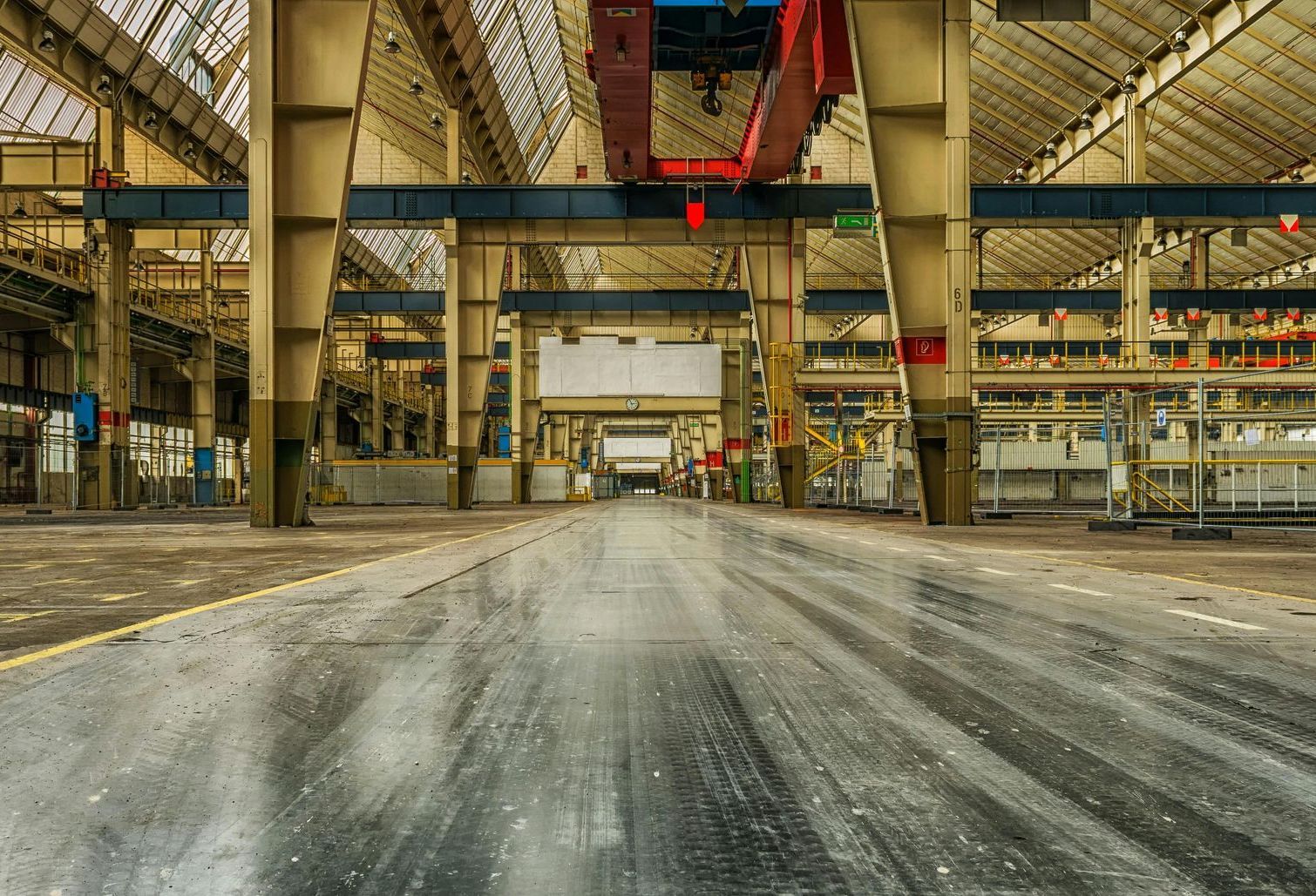 An empty factory with a crane in the middle of it.
