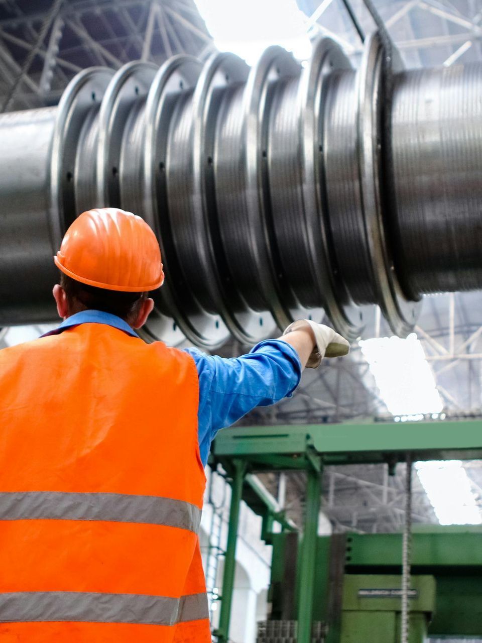 A man wearing an orange vest and hard hat is working on a large pipe