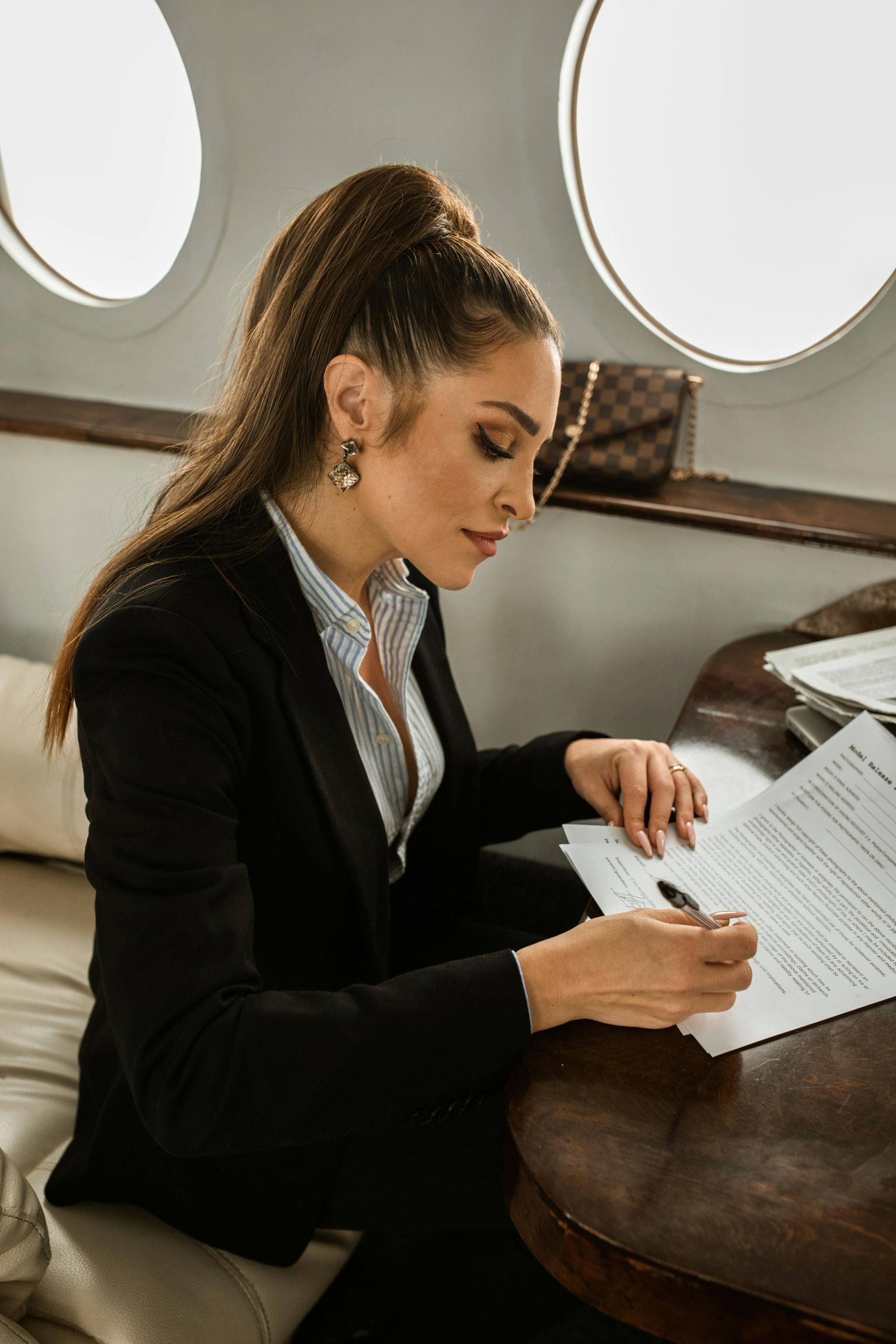 A woman in a suit is sitting at a table in an airplane writing on a piece of paper.