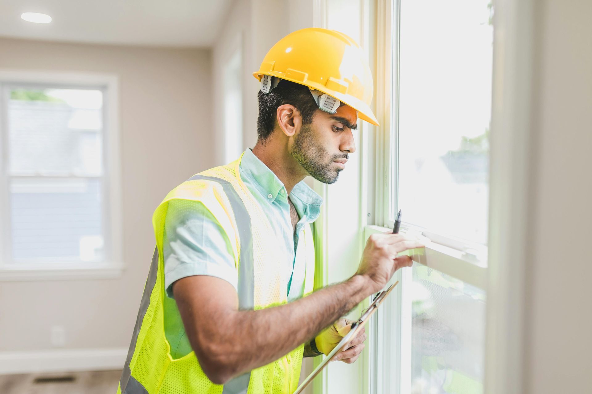 A construction worker is looking out of a window while holding a clipboard.