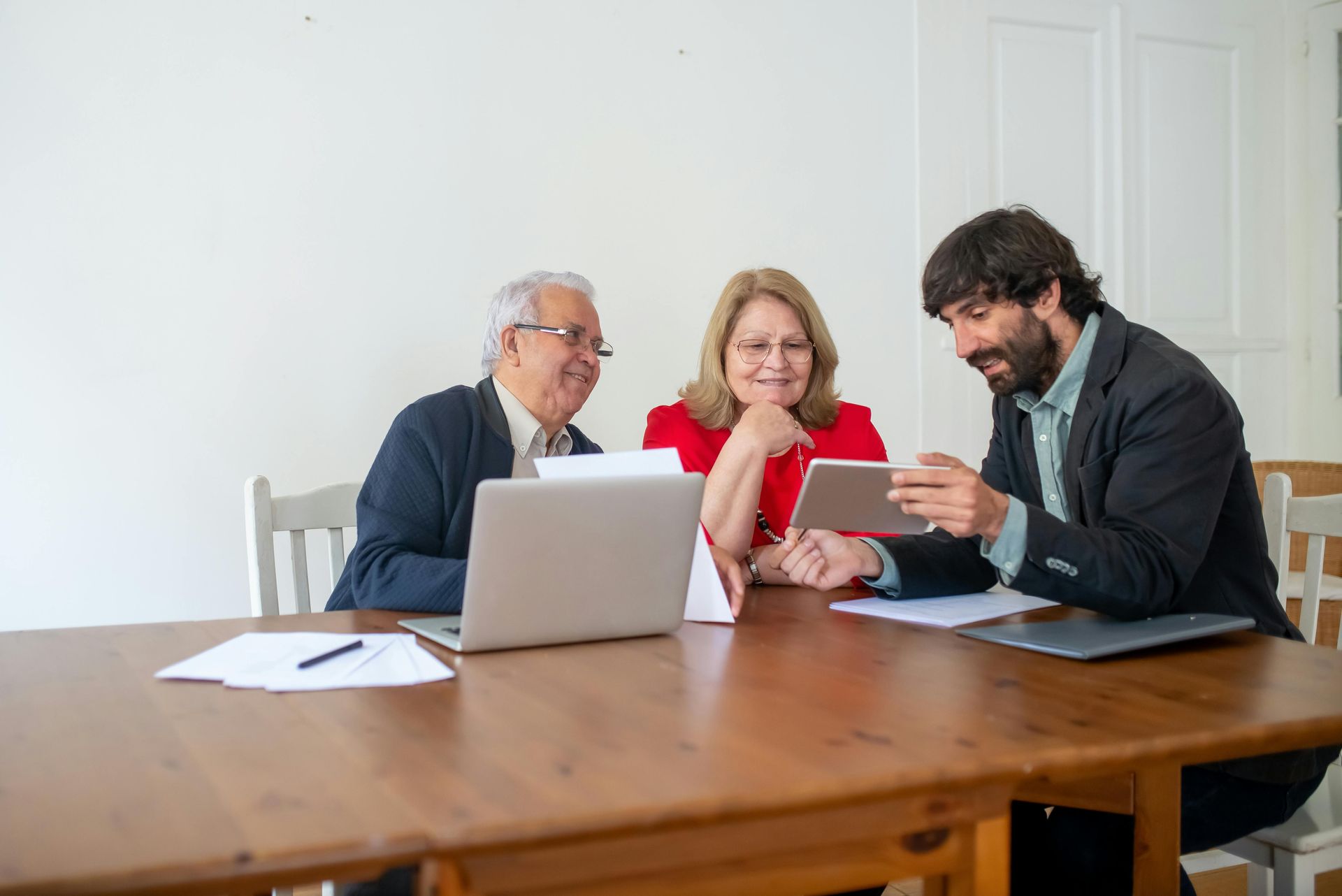 A man is sitting at a table with two older people looking at a tablet.