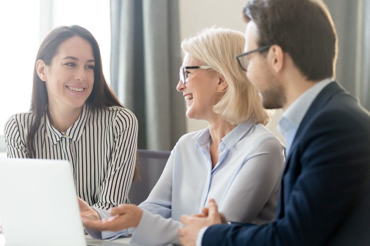 A group of people are sitting around a table looking at a laptop computer.