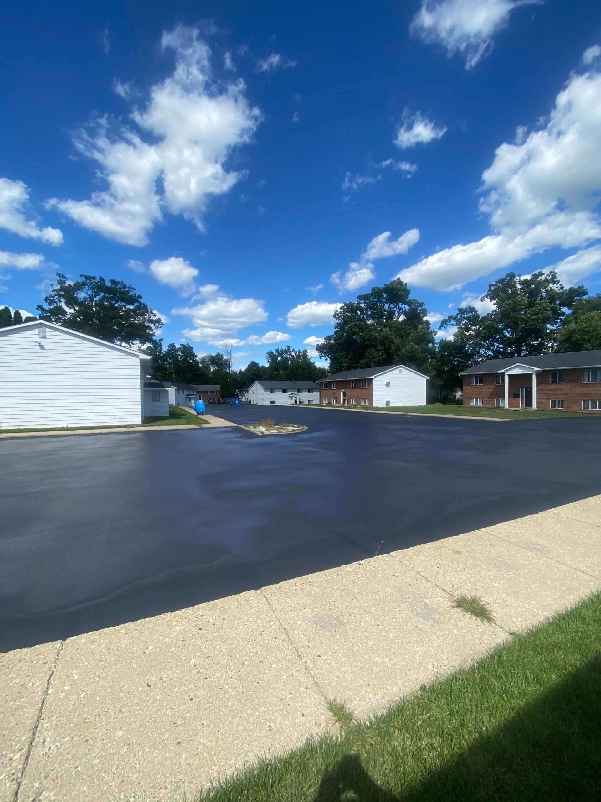 A parking lot with a sidewalk and houses in the background on a sunny day.