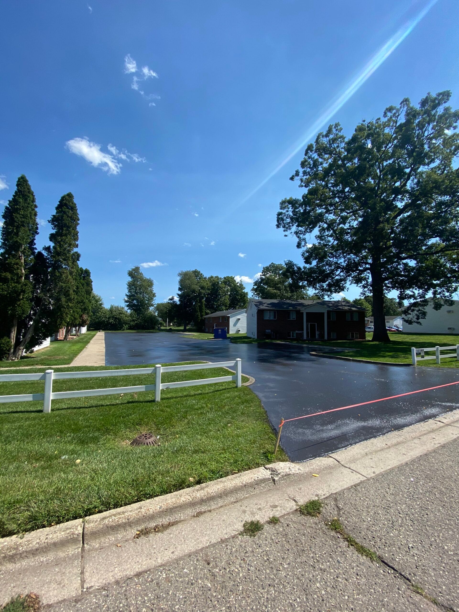 A driveway with a white fence and a house in the background