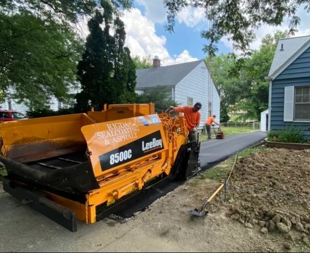 A yellow asphalt paving machine is parked in front of a house.