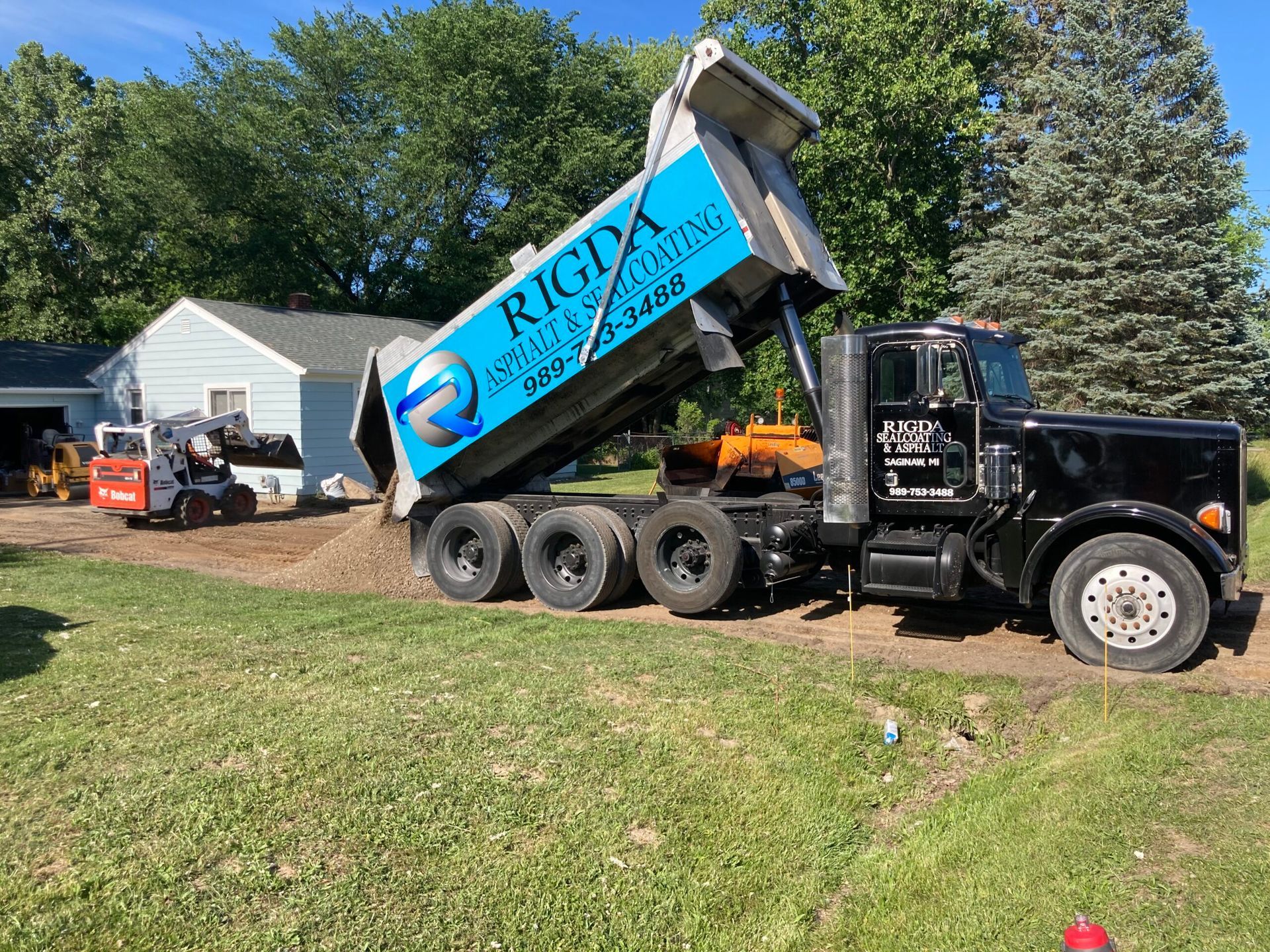 A dump truck is being loaded with dirt in front of a house.