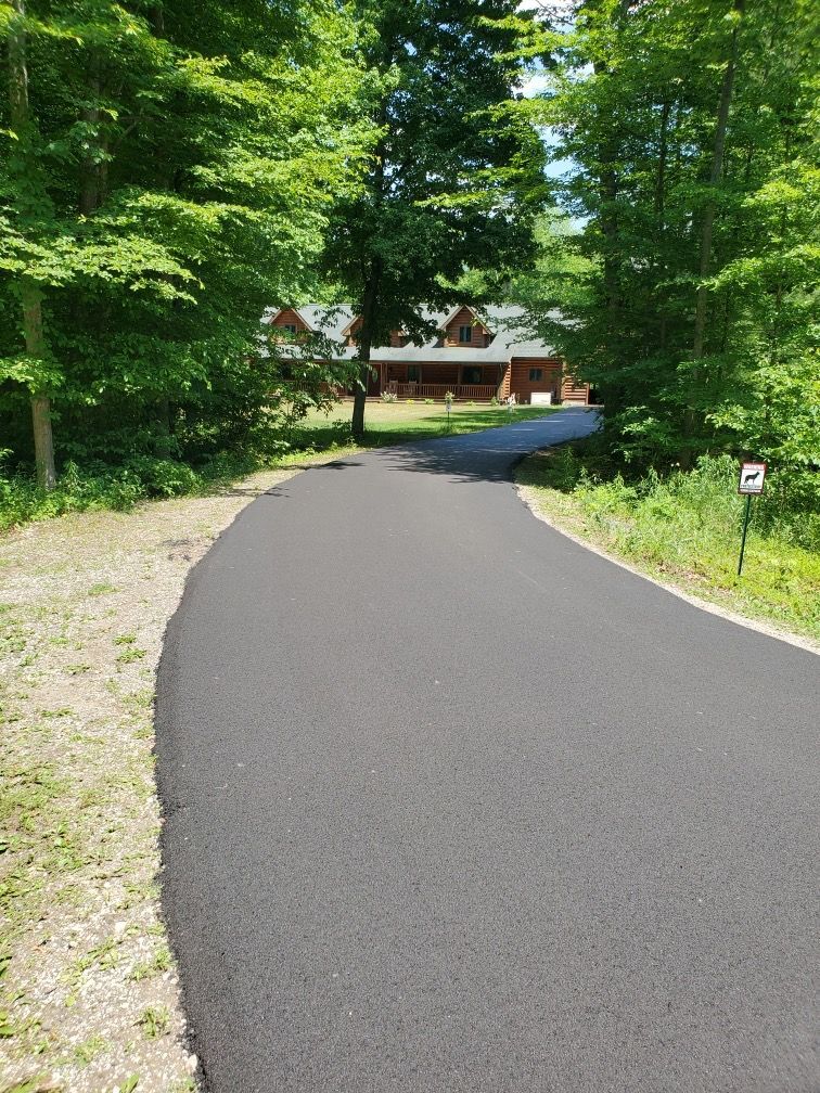 A black asphalt driveway leading to a house in the woods.