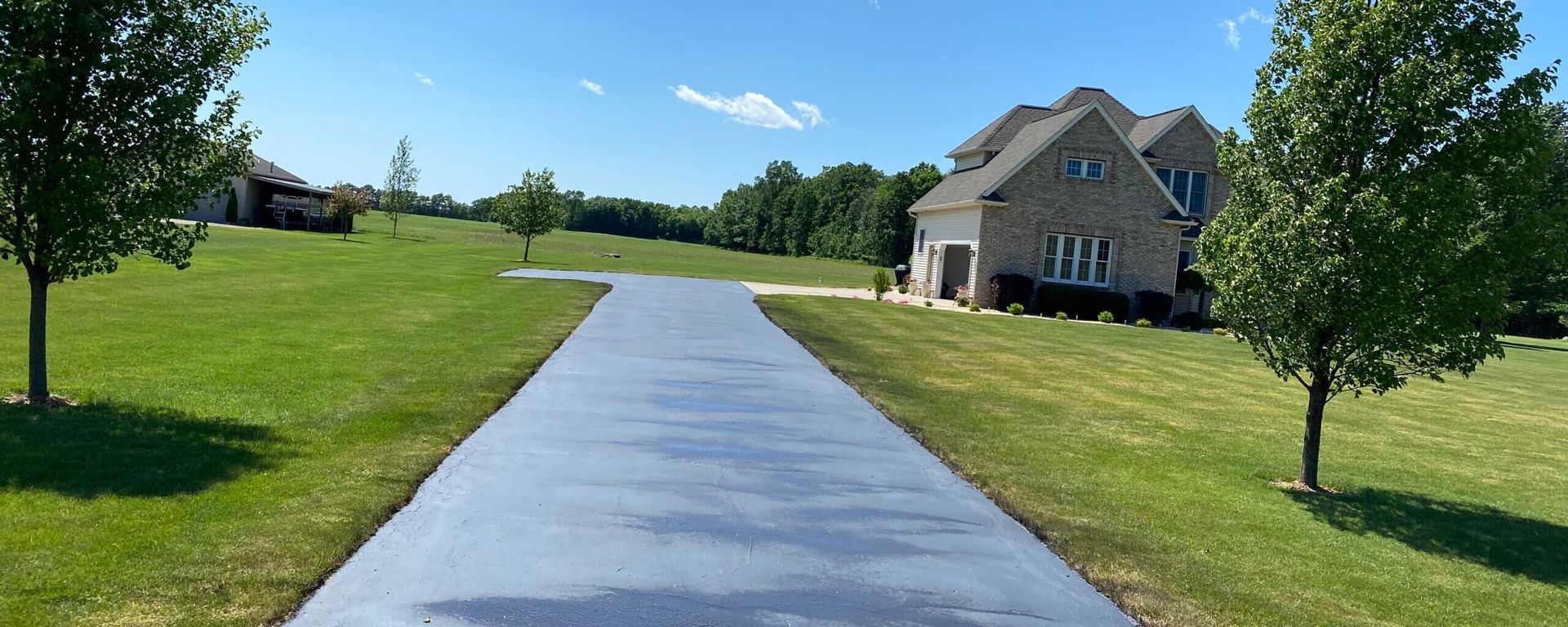 A concrete driveway leading to a large house surrounded by grass and trees.