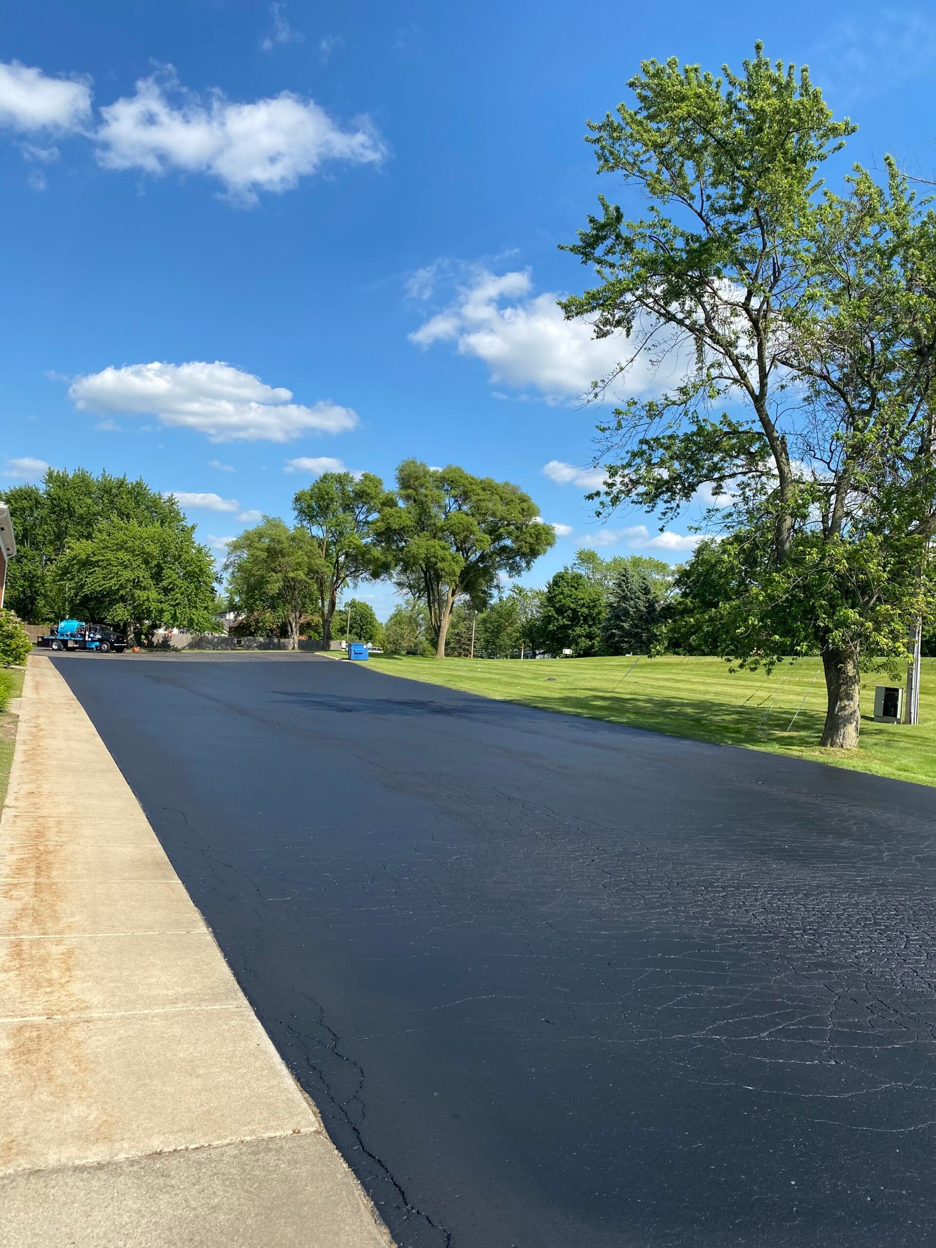 A black asphalt road with trees on both sides and a blue sky in the background.