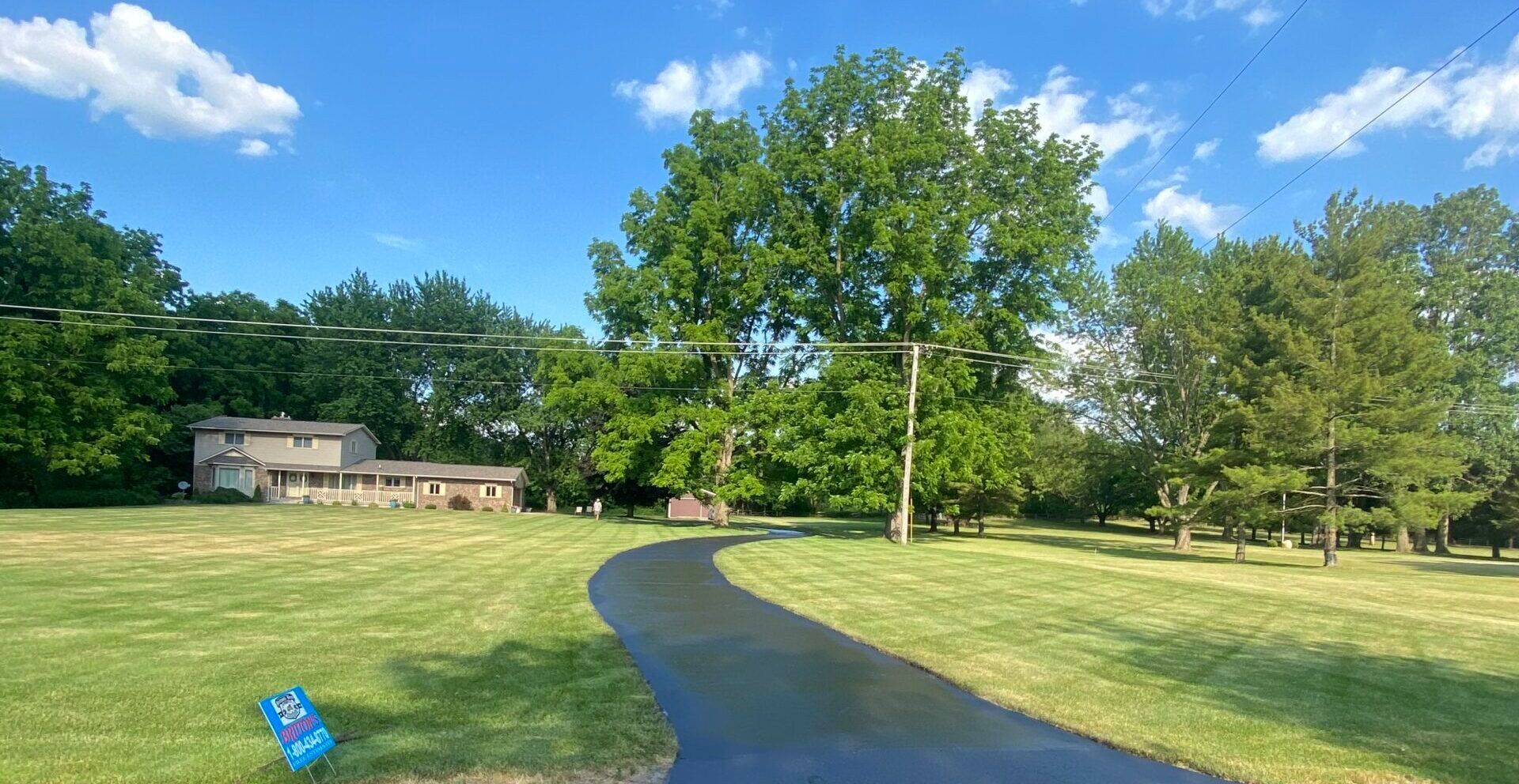 A driveway leading to a house in the middle of a lush green field.