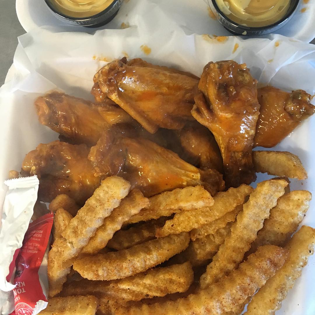 Chicken wings with fries and dipping sauces in a foam container.