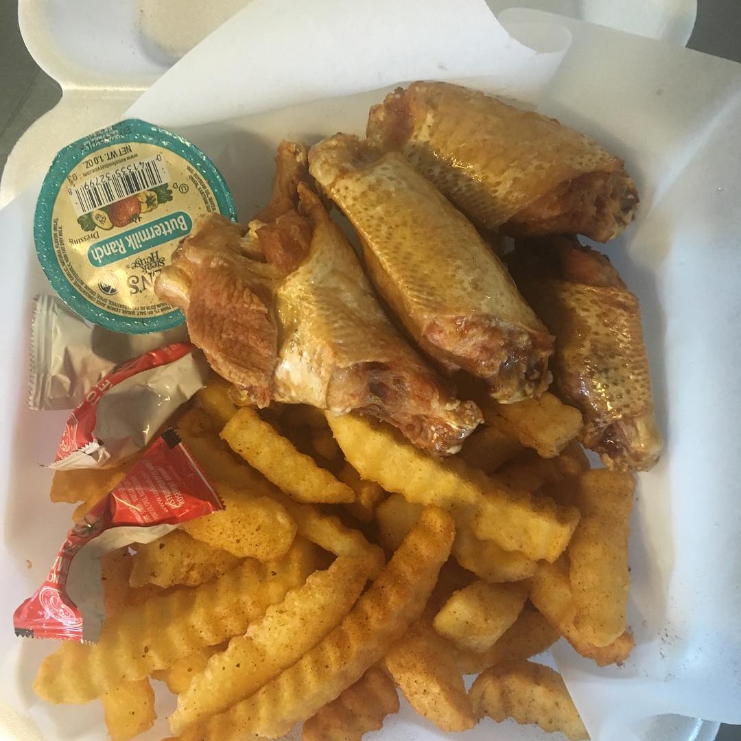Chicken wings, crinkle fries, and dipping sauce in a white takeout container.