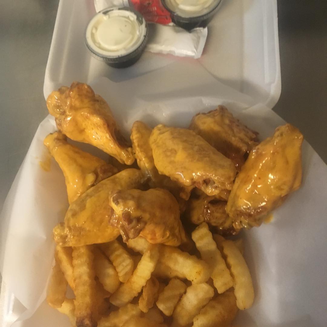 Buffalo wings and fries in a to-go container with dipping sauces.