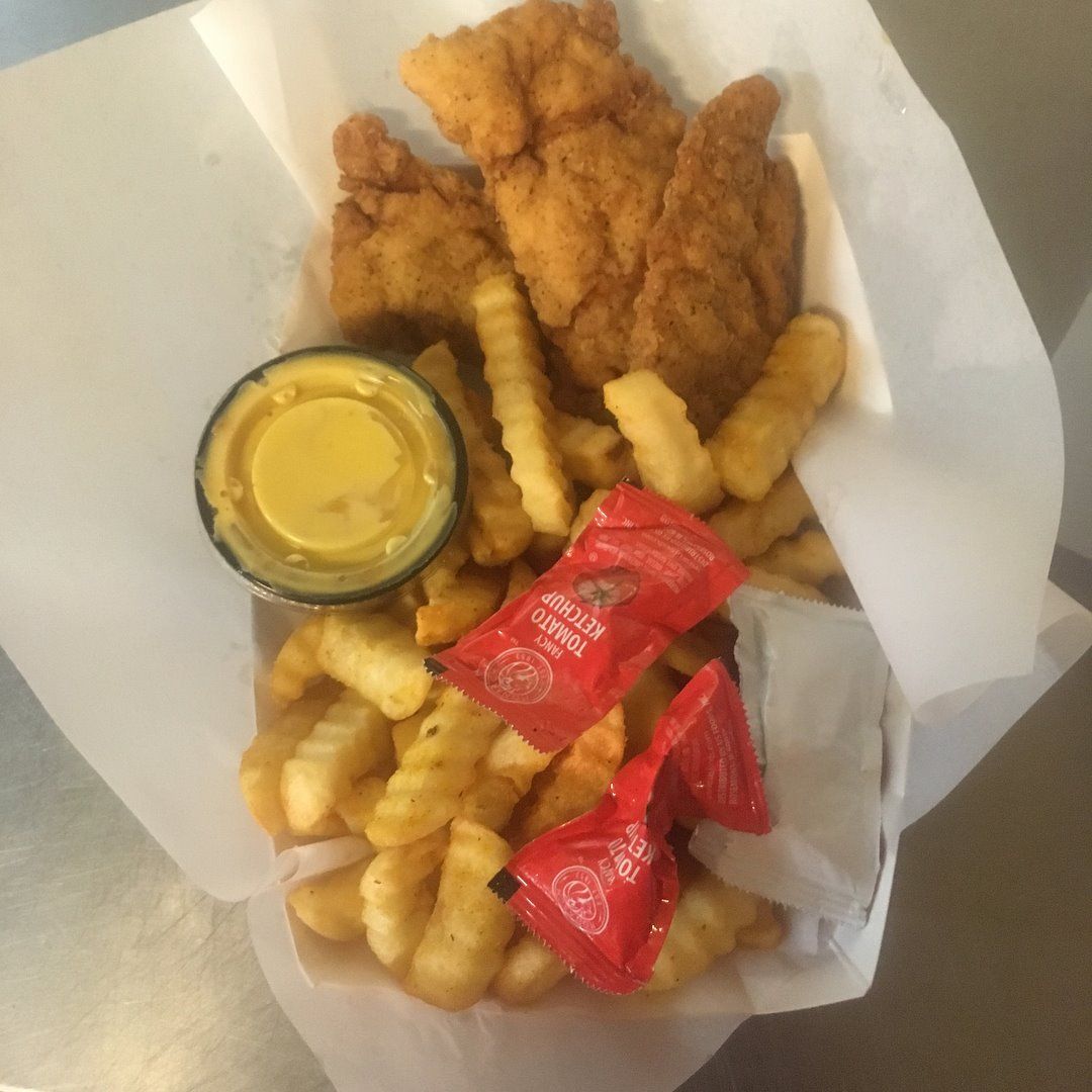 Chicken tenders and fries in a basket, with dipping sauce and ketchup packets.