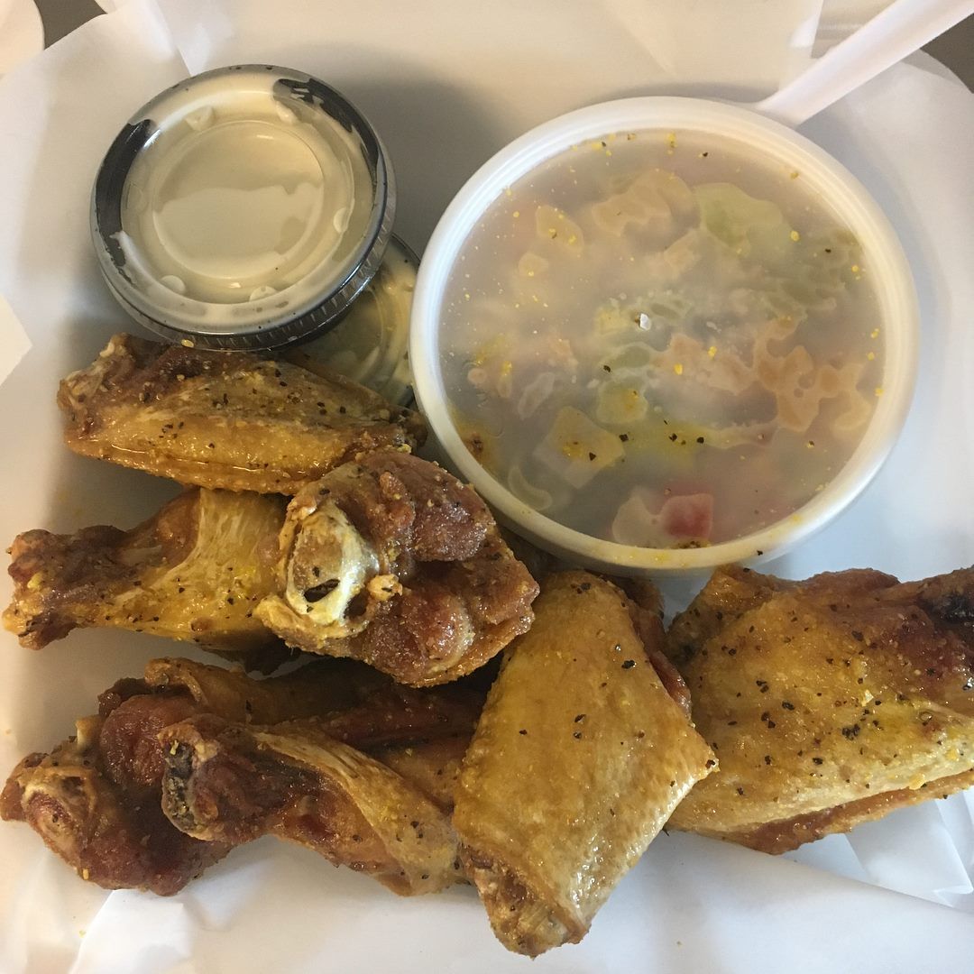 Fried chicken wings, potato salad, and ranch dressing in a takeout container.