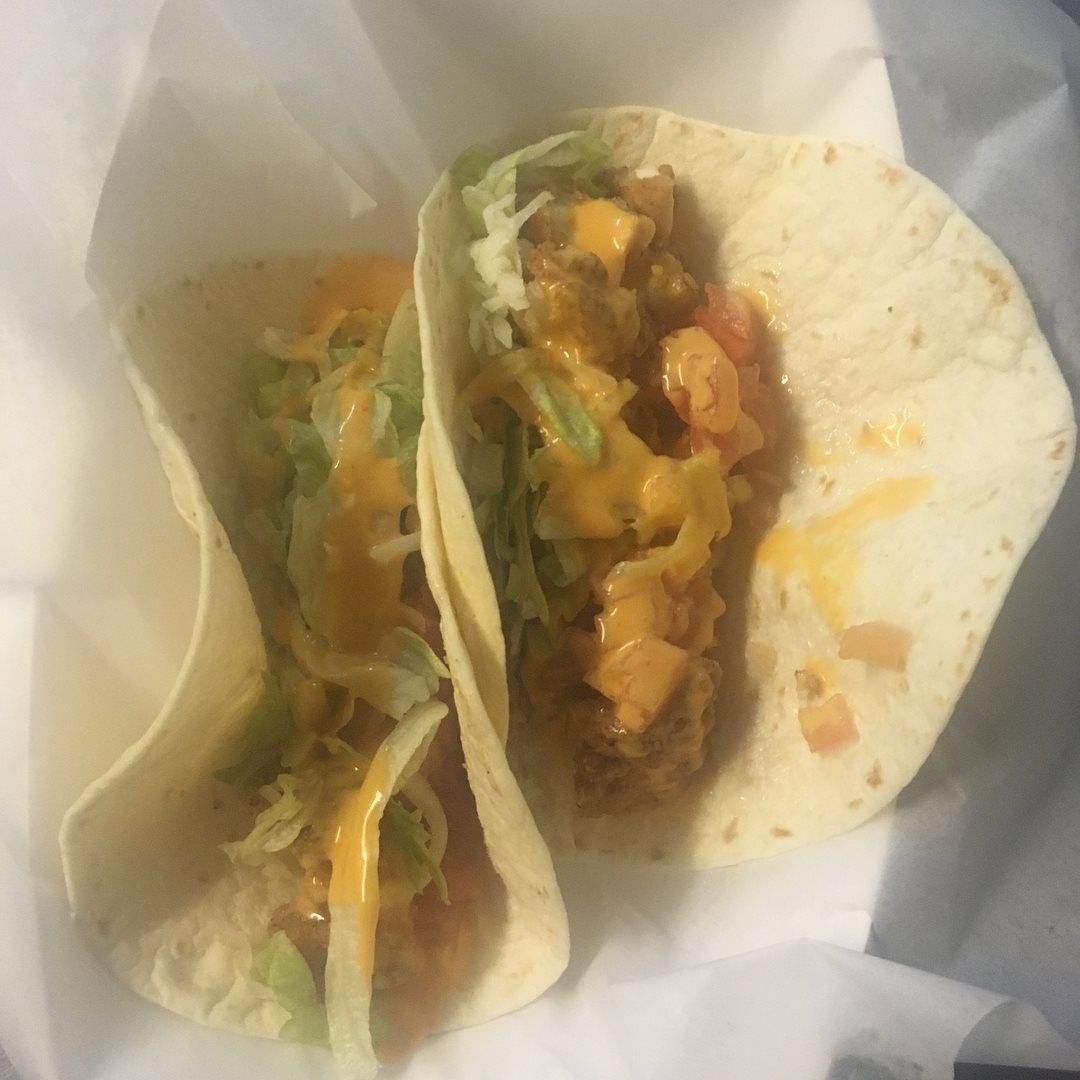 Two tacos in soft tortillas, filled with meat, lettuce, cheese, and sauce.