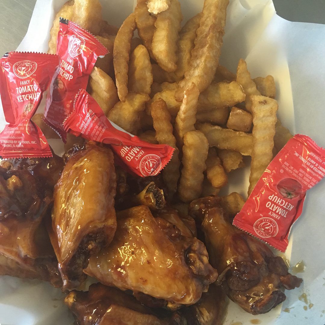 Chicken wings and fries with ketchup packets in a basket.