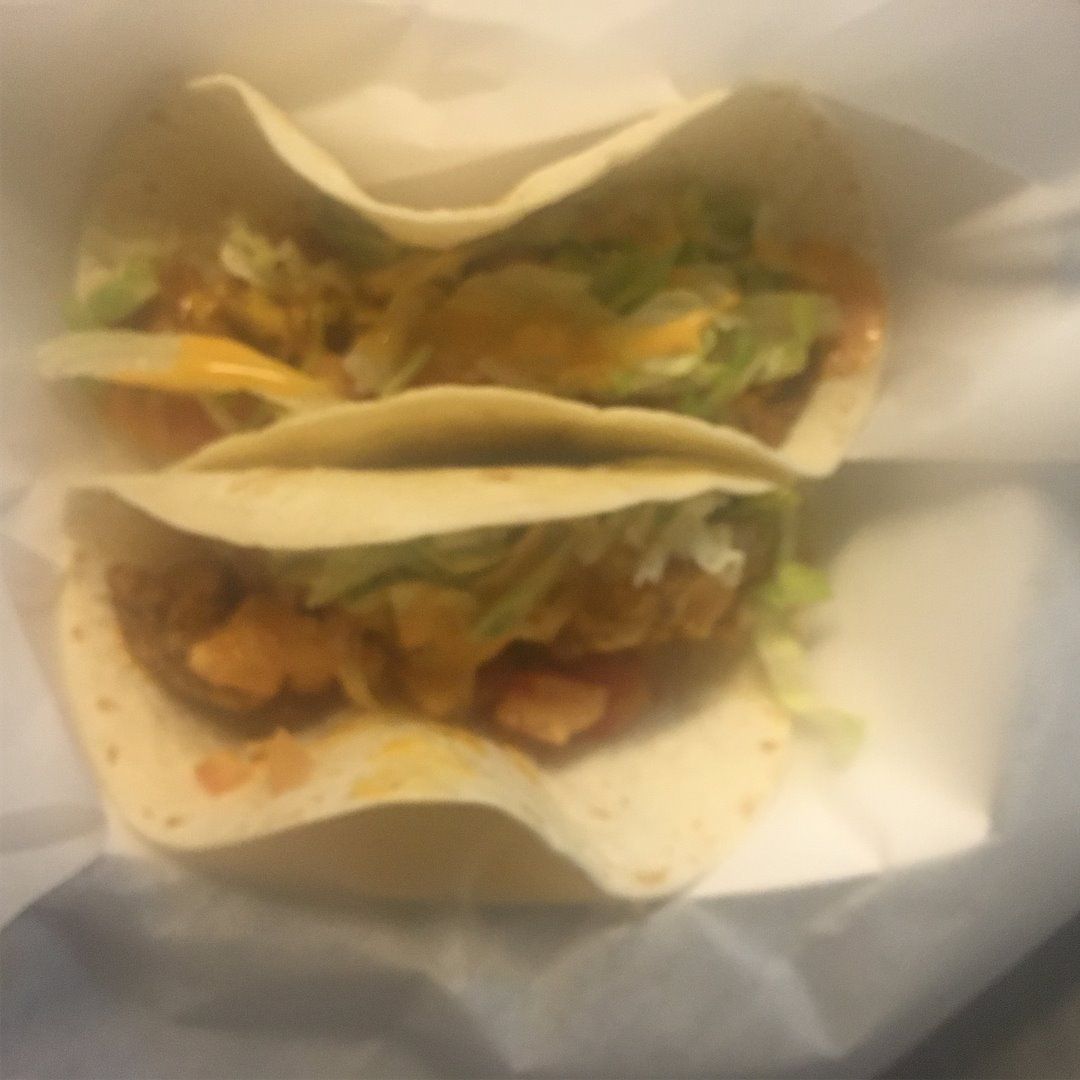 Two tacos stacked, filled with meat, lettuce, cheese, and sauce.