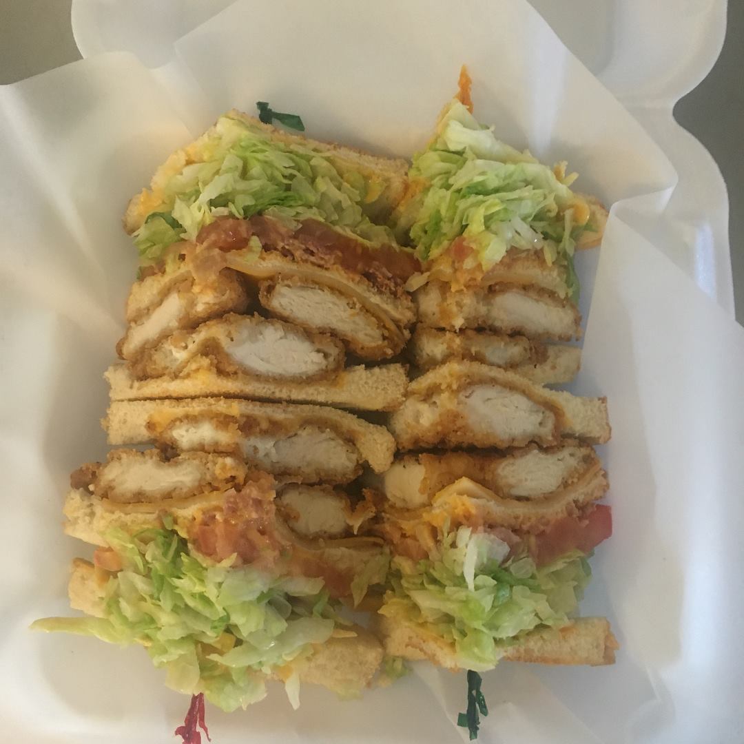 Chicken sandwich with lettuce, tomato, and bacon, in a white container.