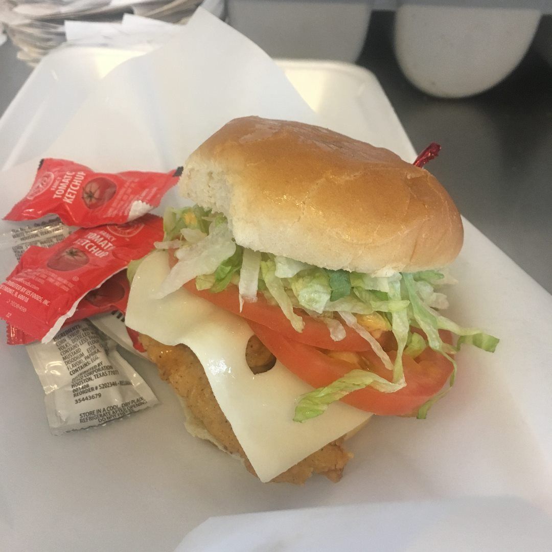 Chicken sandwich with cheese, tomato, lettuce on a bun, with ketchup packets.