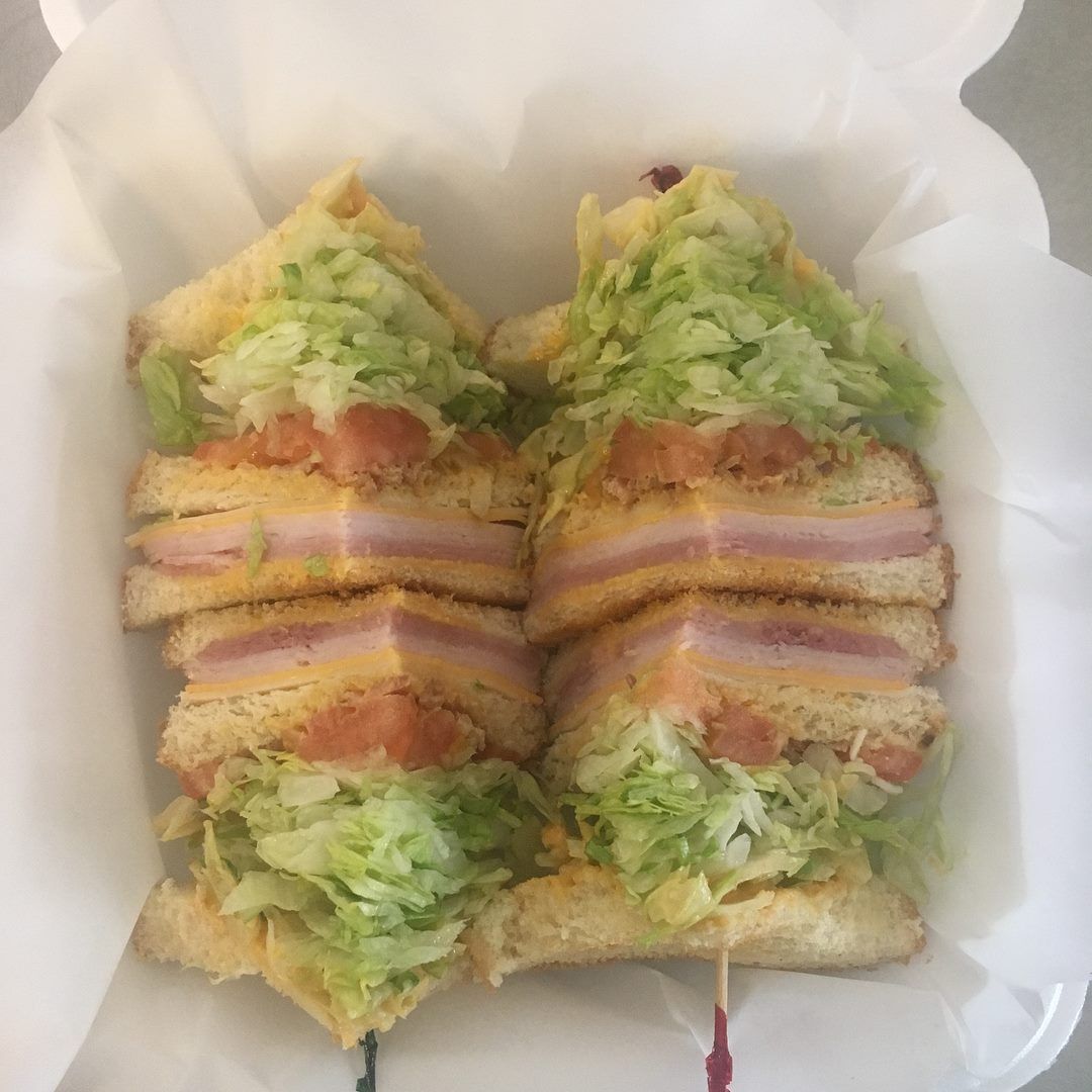Two club sandwiches cut in half, stacked in a white container with lettuce, tomato, cheese, and ham.