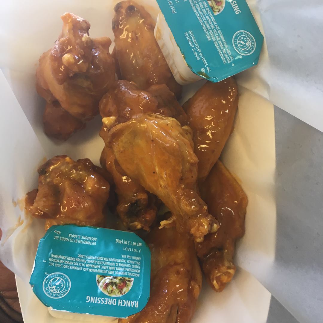 Chicken wings with orange sauce, two ranch dressing cups, white paper, top view.